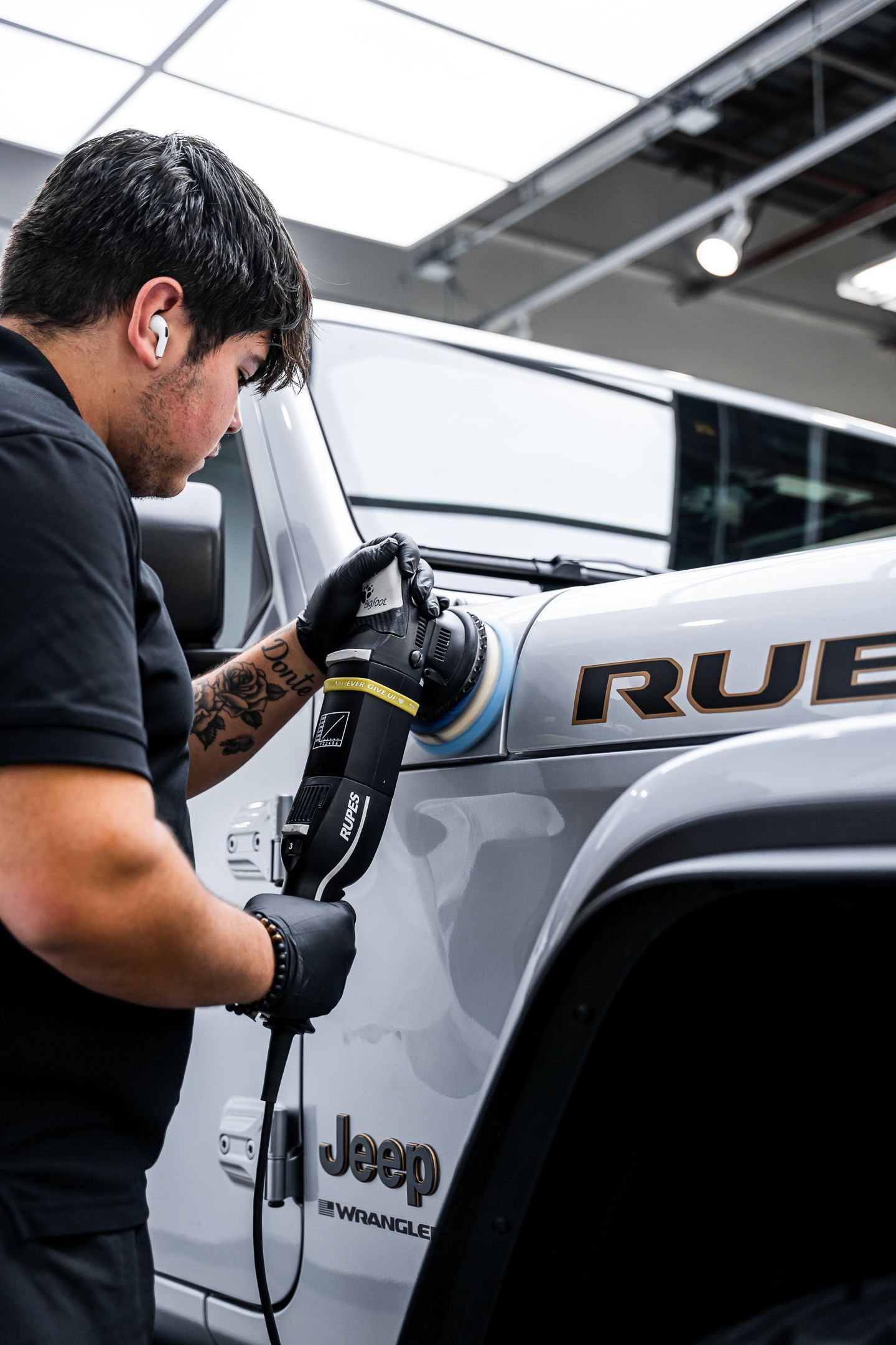 A man is polishing the hood of a jeep wrangler.