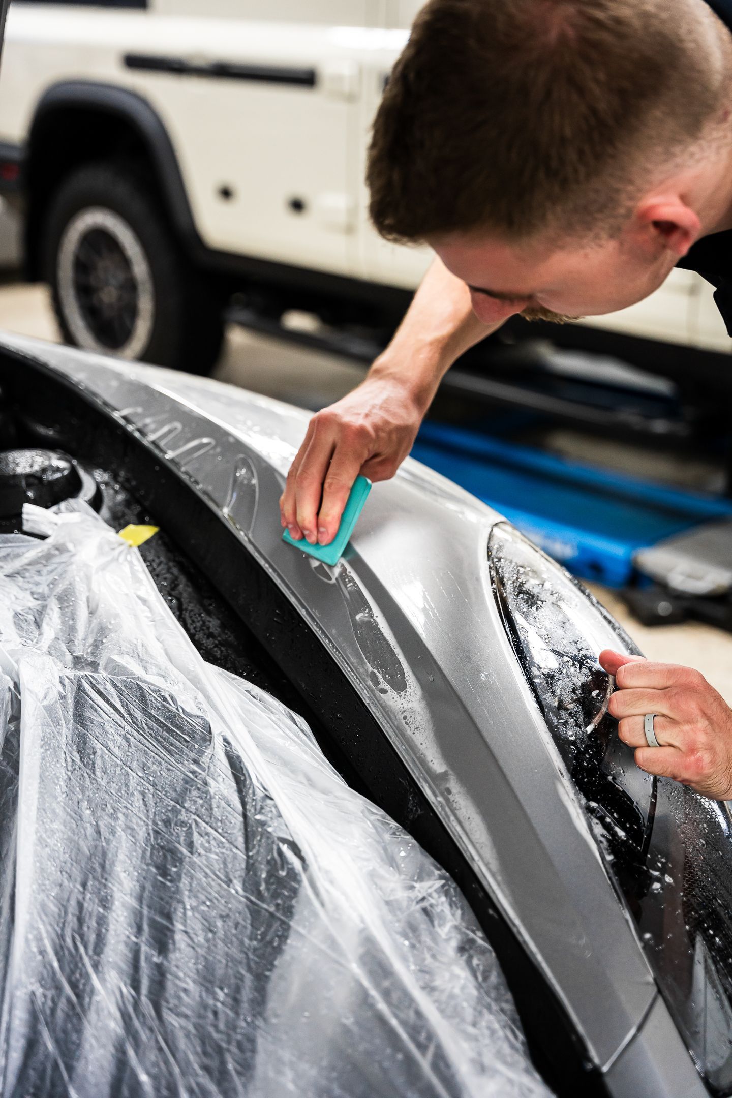 A man is cleaning the hood of a car with a sponge.