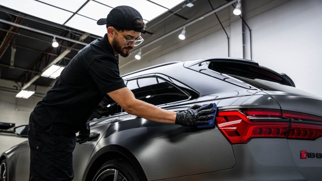 A man is cleaning a car with a cloth in a garage.