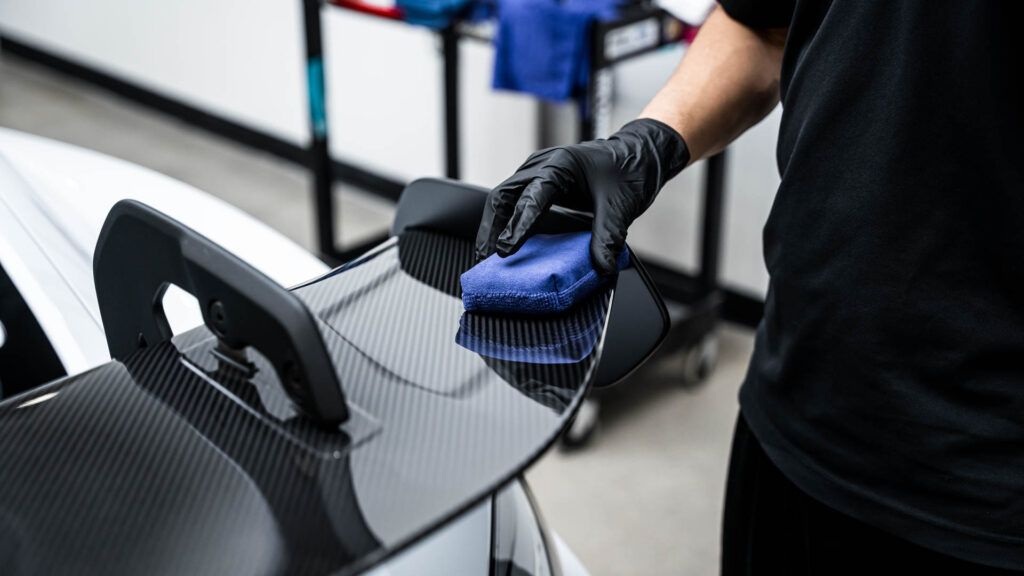 A person is cleaning the spoiler of a car with a cloth.