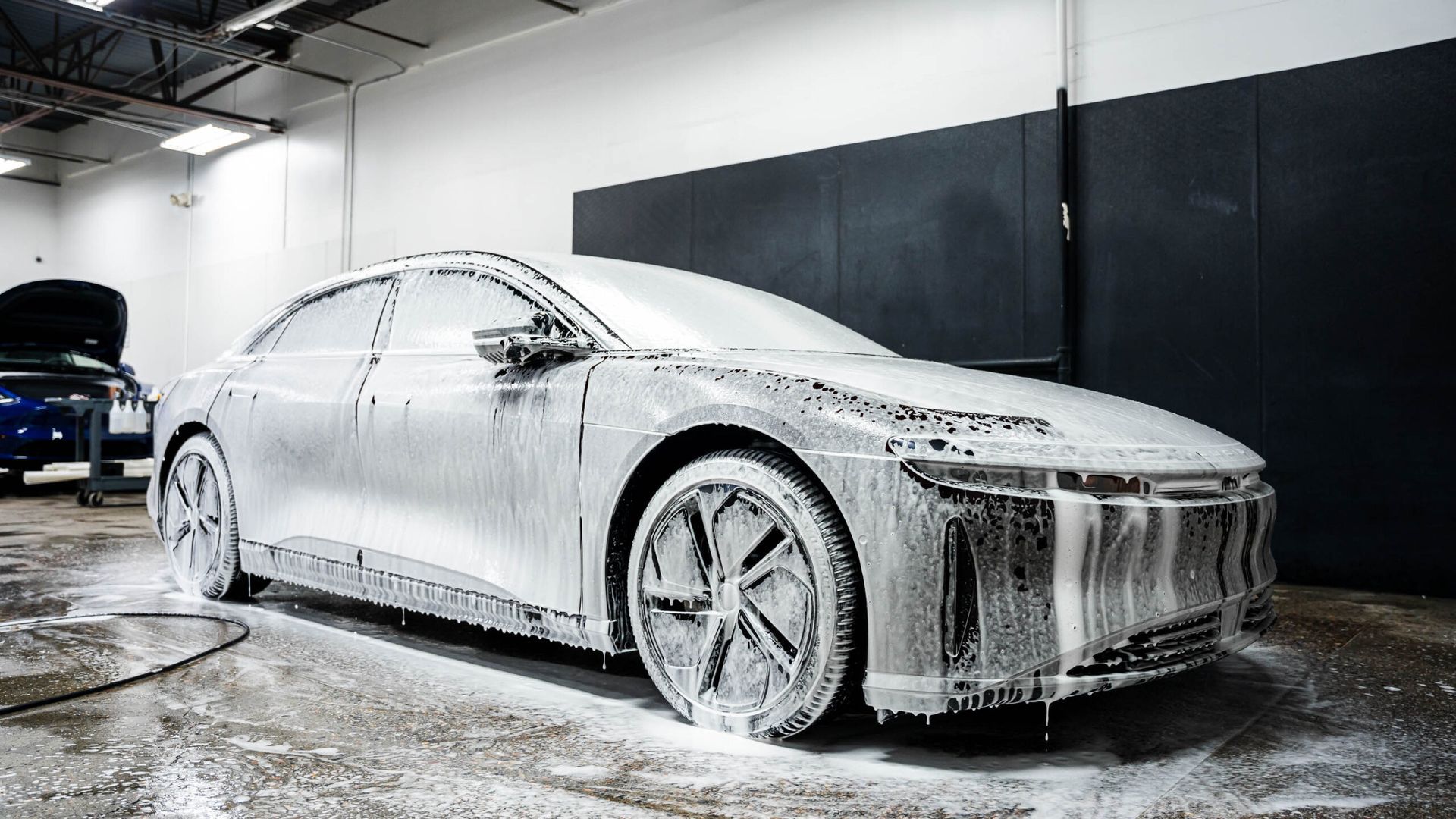 A white car is covered in foam in a garage.