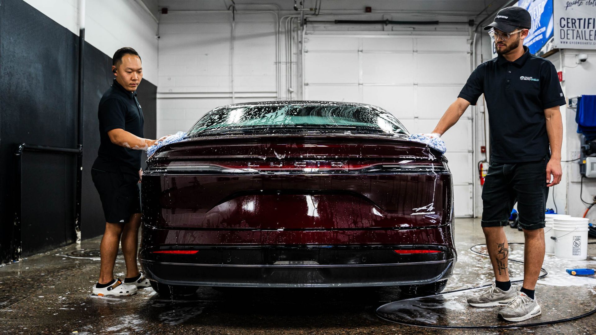 Two men are washing a red car in a garage.