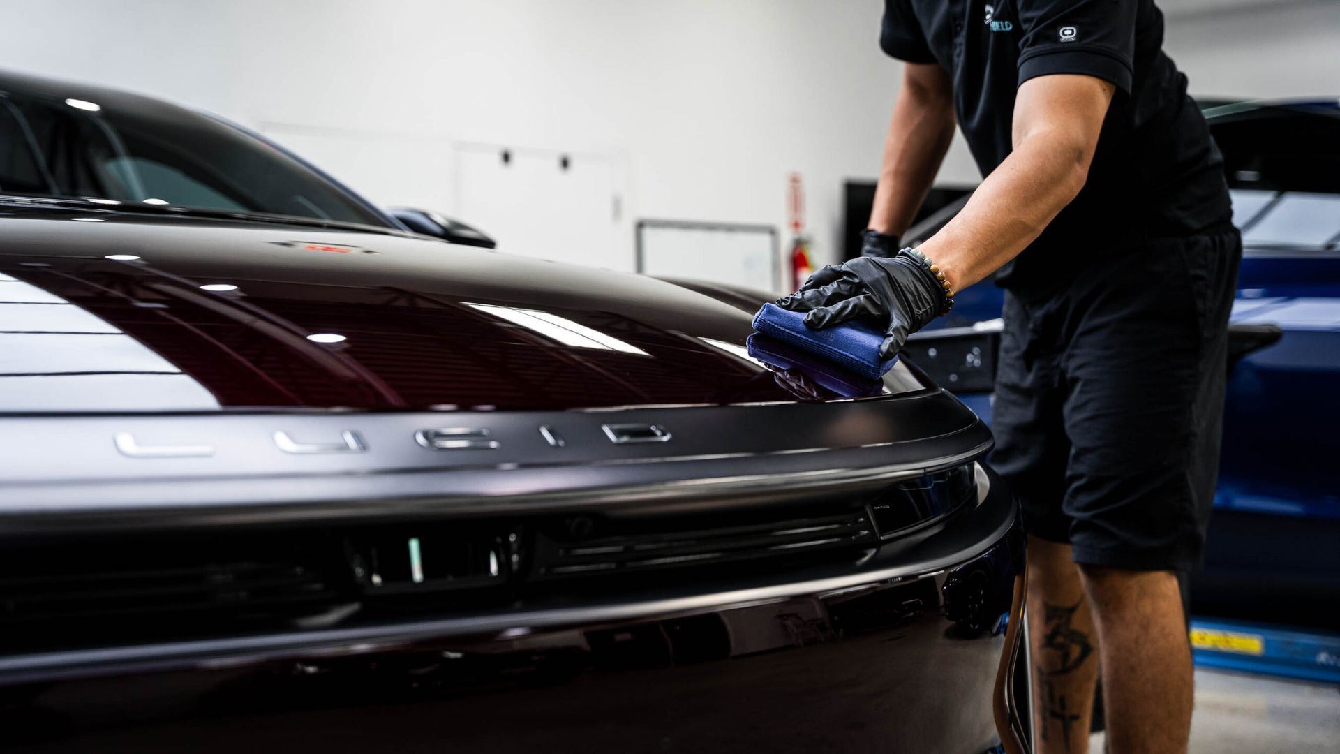 A man is polishing the hood of a black car in a garage.