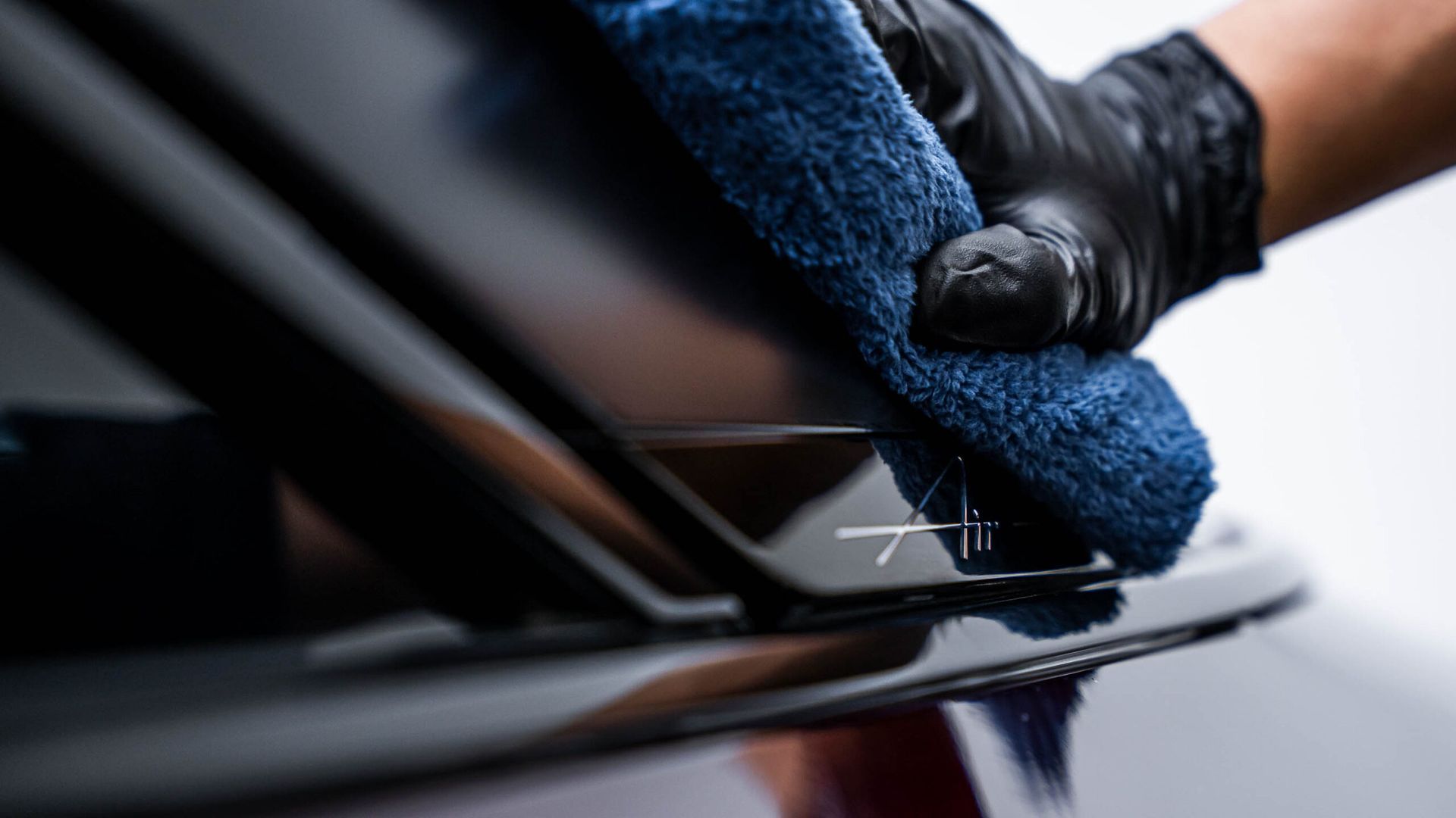 A person wearing black gloves is cleaning a car with a blue cloth.