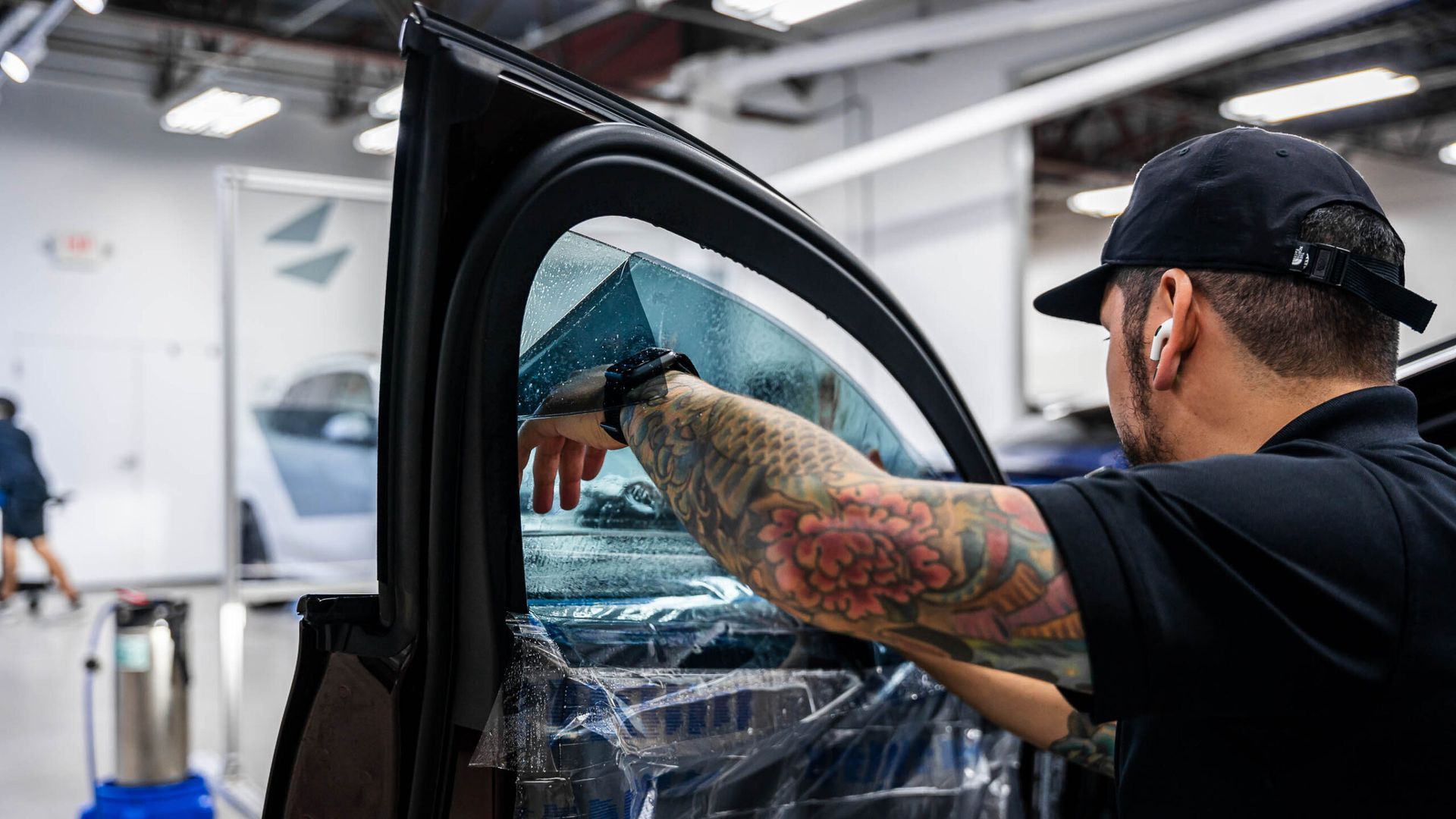 A man with tattoos is applying window tinting to a car window.