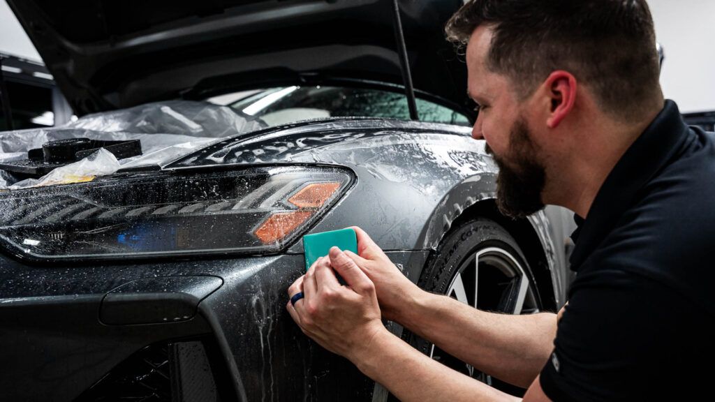 A man is applying protective film to the front of a car.