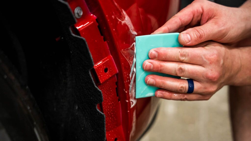 A person is cleaning a red car with a sponge.