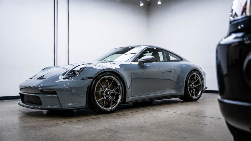 A grey porsche 911 is parked in a garage next to a black car.