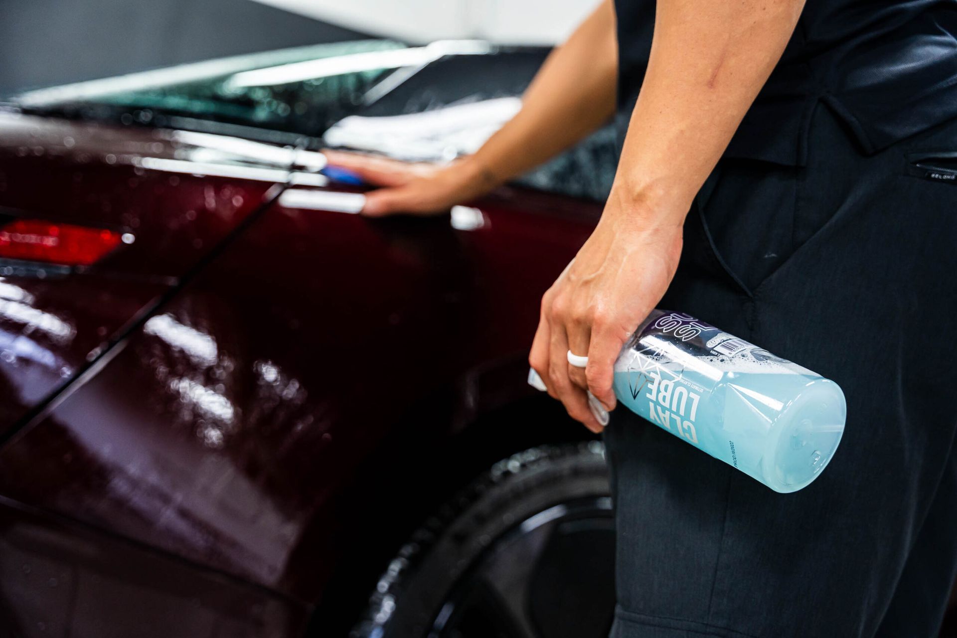 A person is holding a bottle of liquid in front of a car.