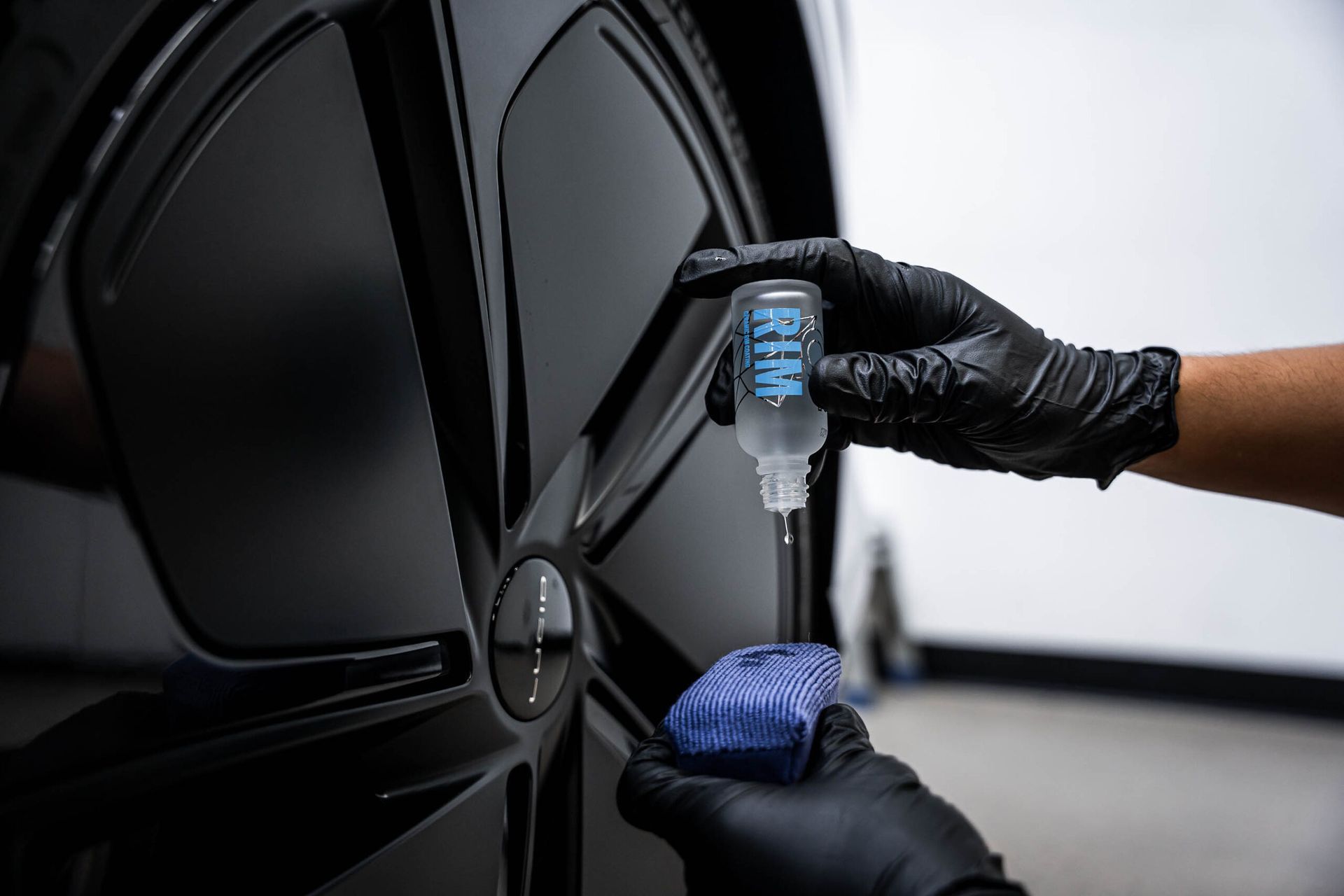 A person wearing black gloves is applying a coating to a car wheel.