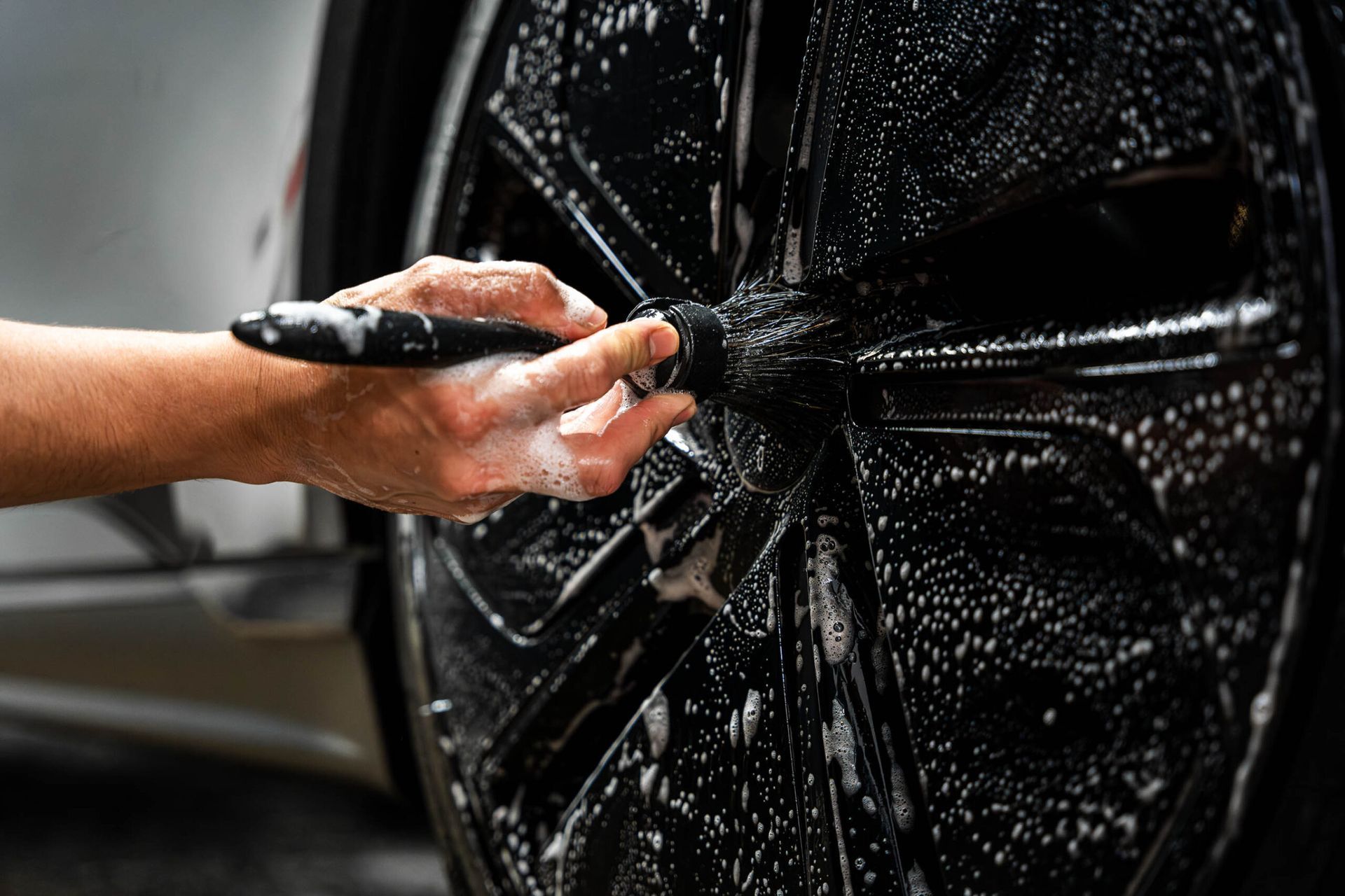 A person is washing a car wheel with a brush.