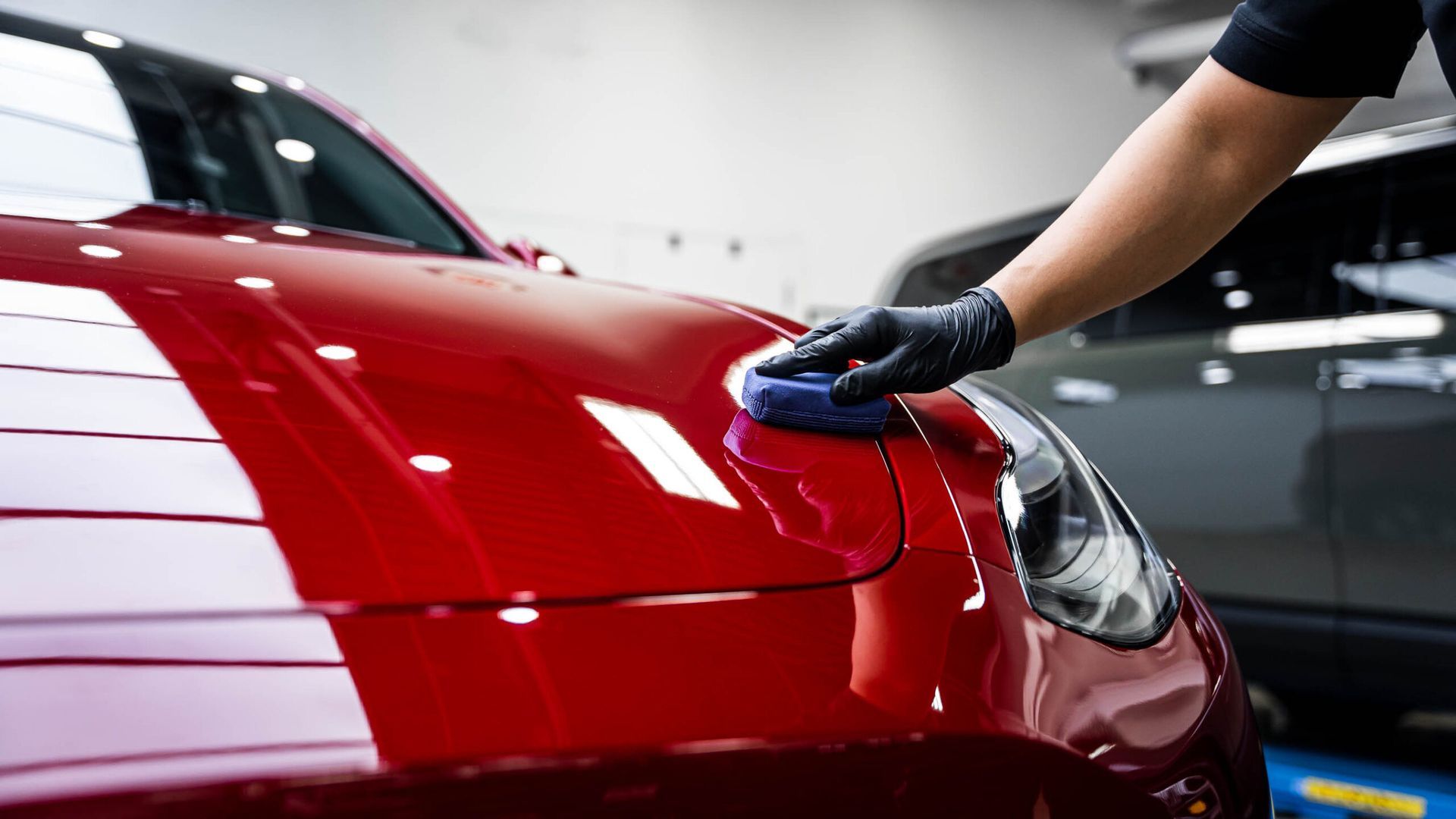 A person is polishing a red car with a sponge.