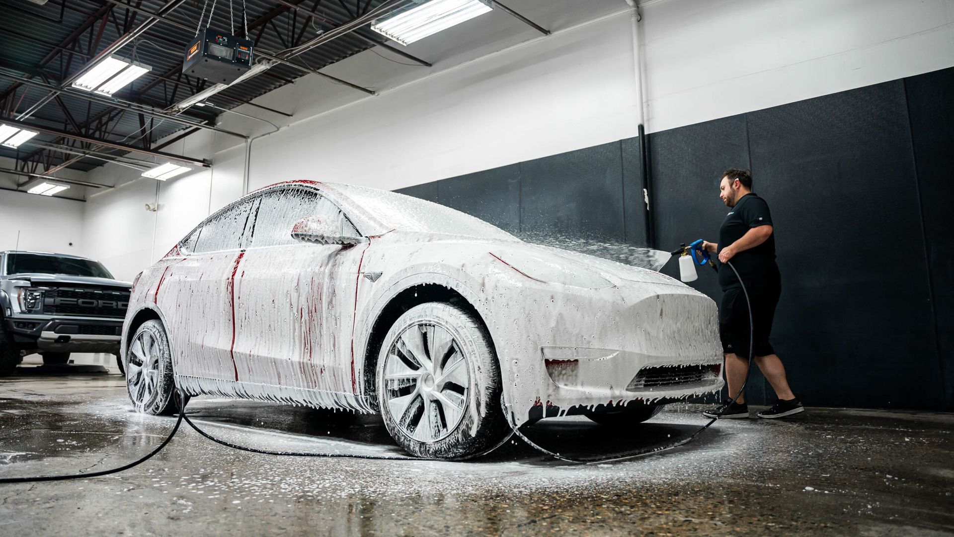 A man is washing a tesla model y with foam in a garage.