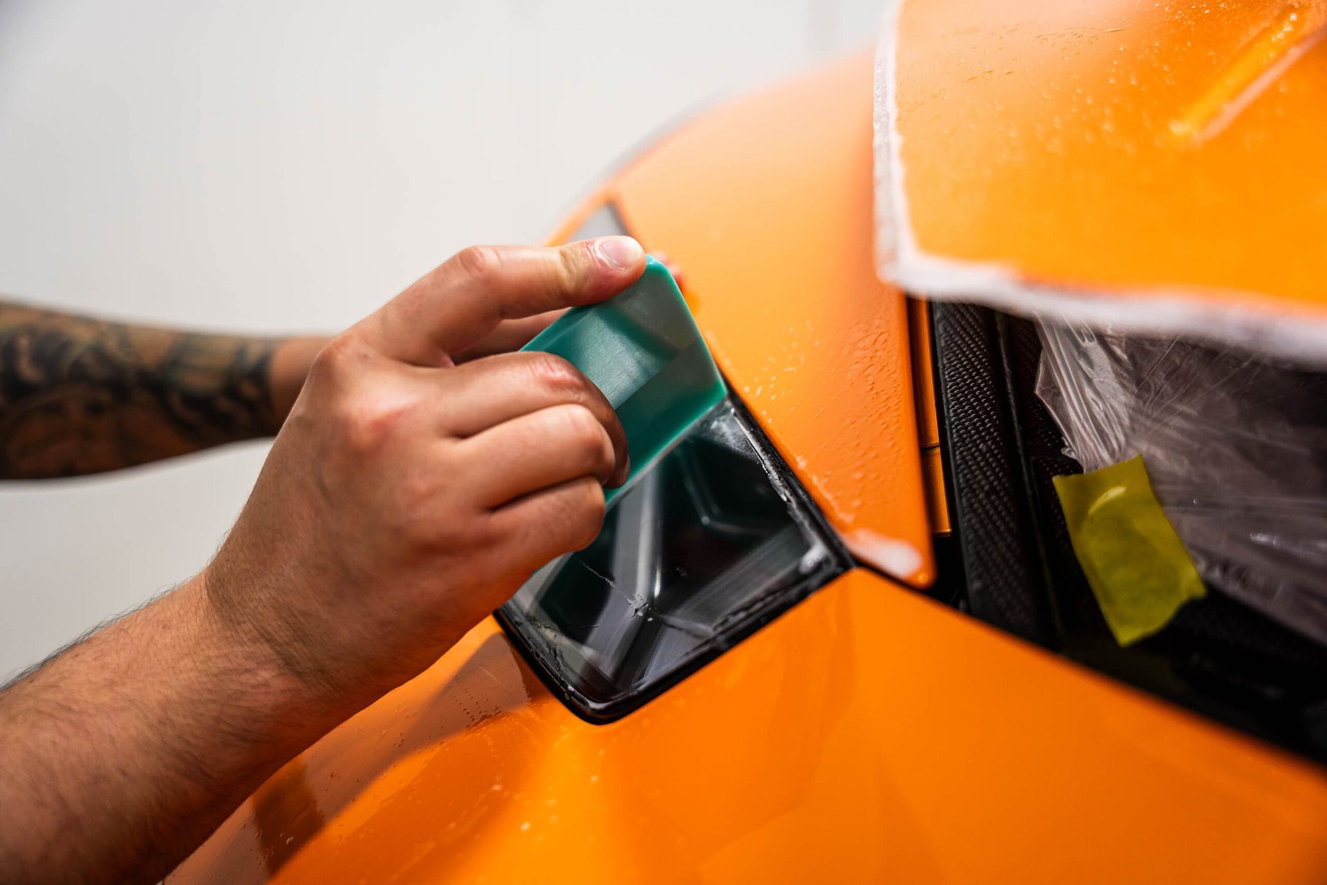 A person is wrapping a car with a green tape.