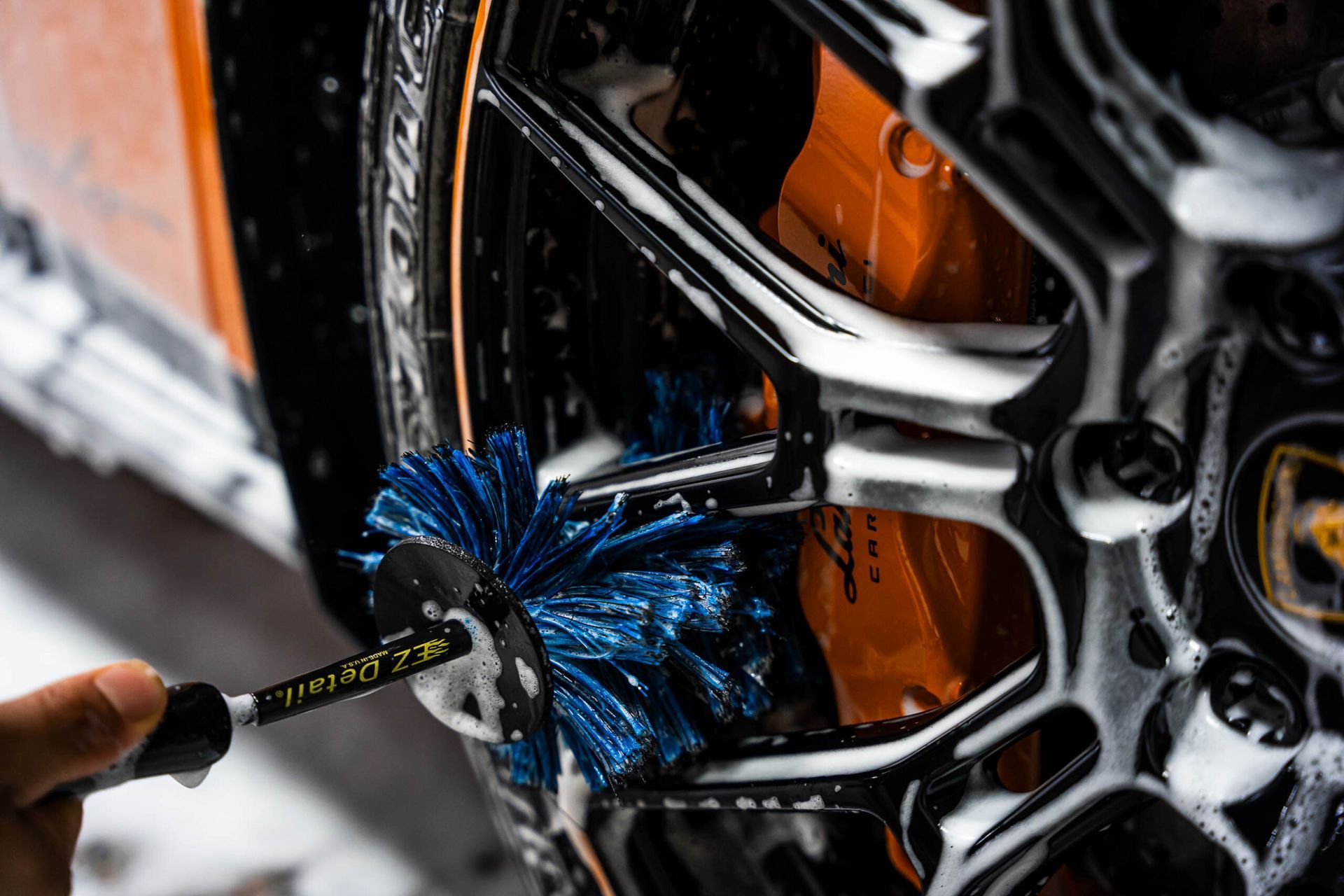 A person is cleaning a car wheel with a brush.