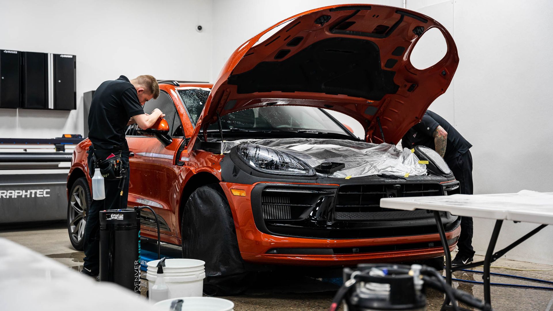 Two men are working on a car in a garage with the hood open.