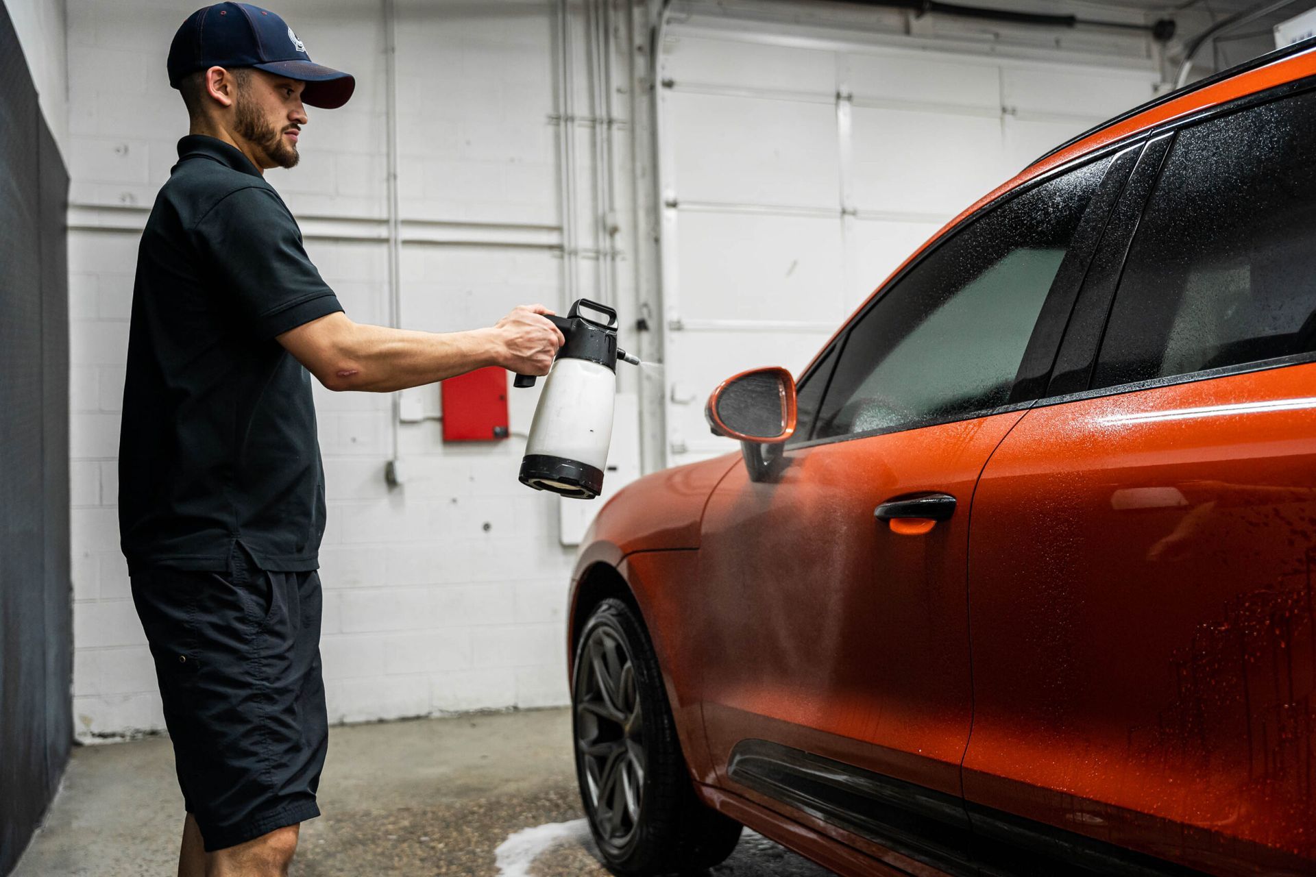 A man is washing a car with a spray bottle in a garage.