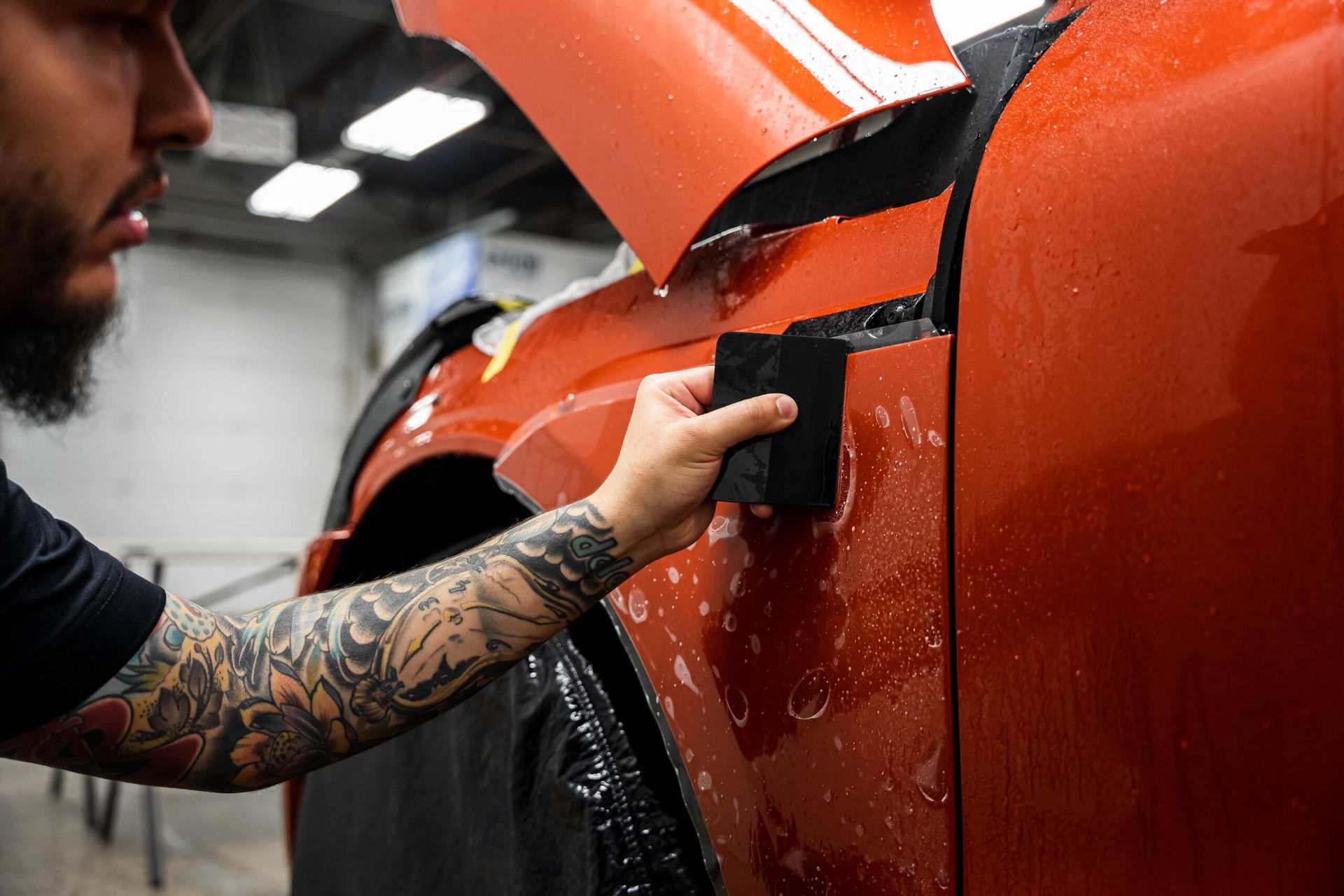 A man is applying a protective film to the side of a car.