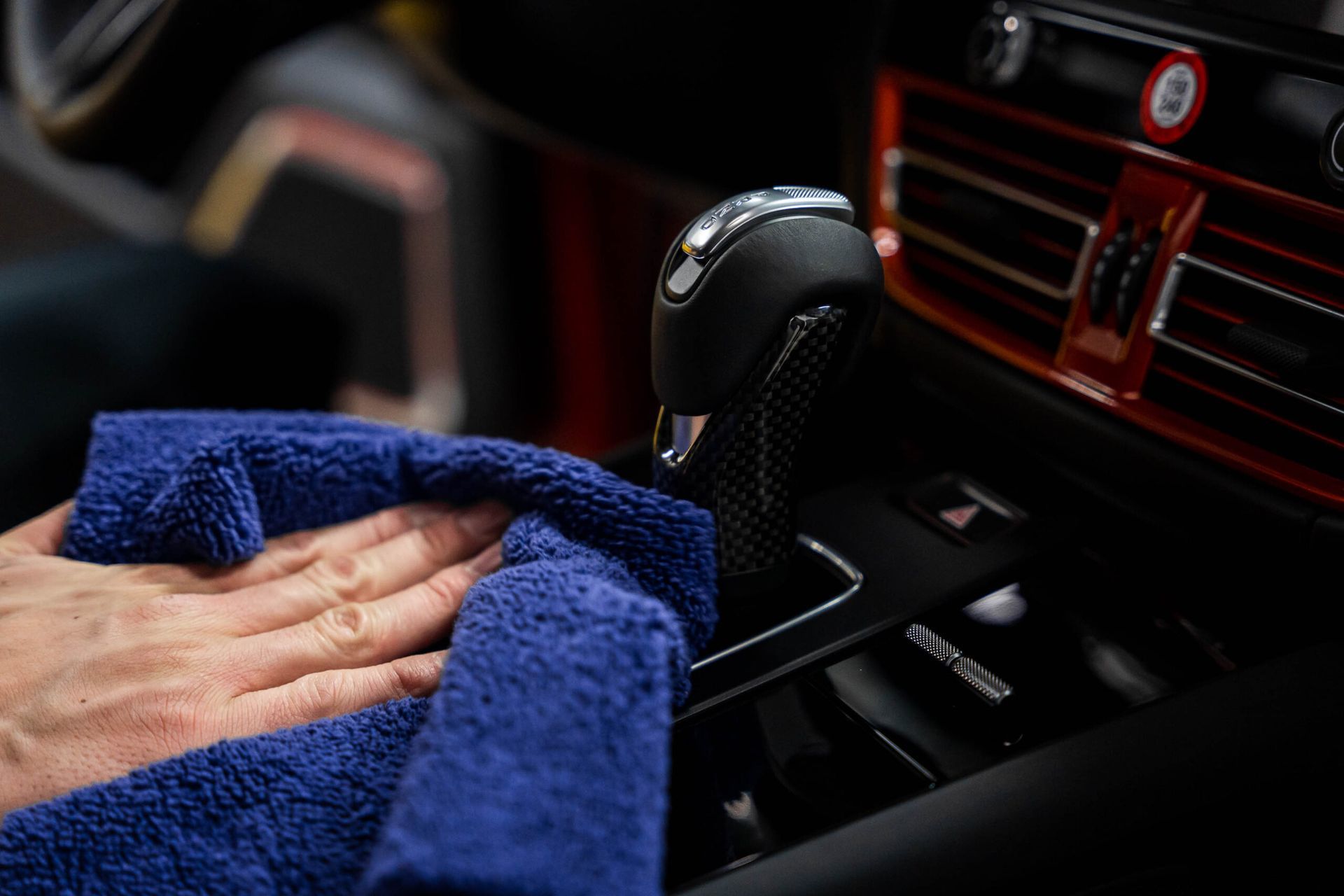 A person is cleaning the dashboard of a car with a blue towel.