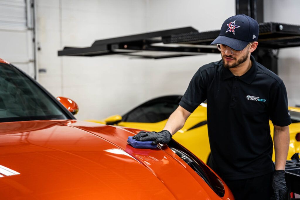 A man is polishing the hood of an orange car in a garage.