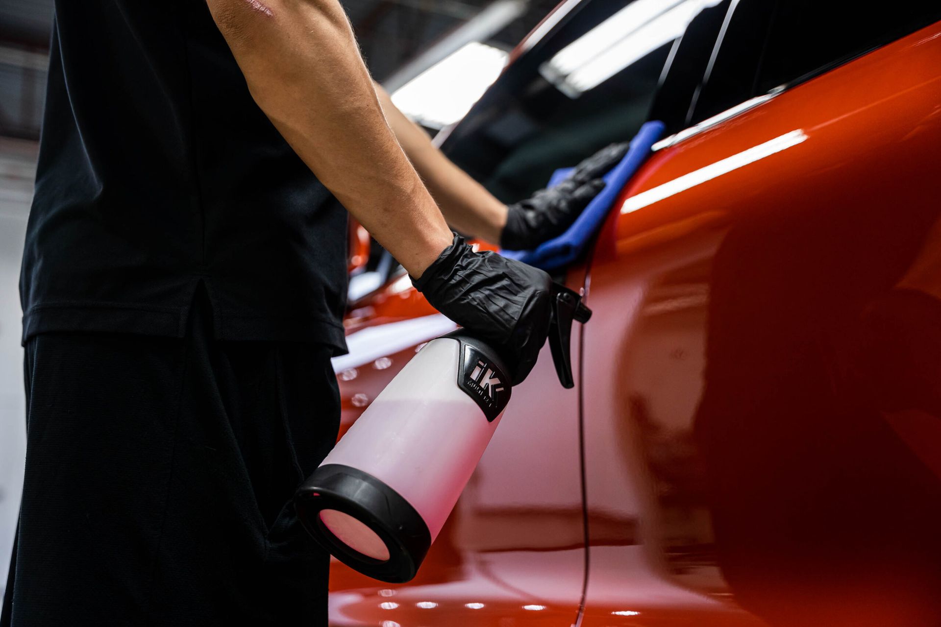 A man is cleaning a red car with a spray bottle.