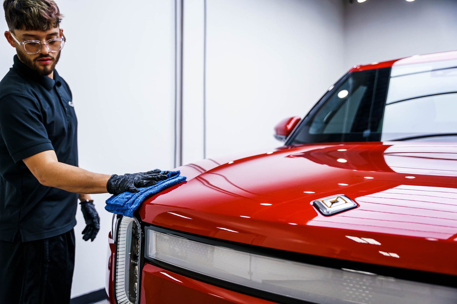 A man is cleaning the hood of a red car with a cloth.