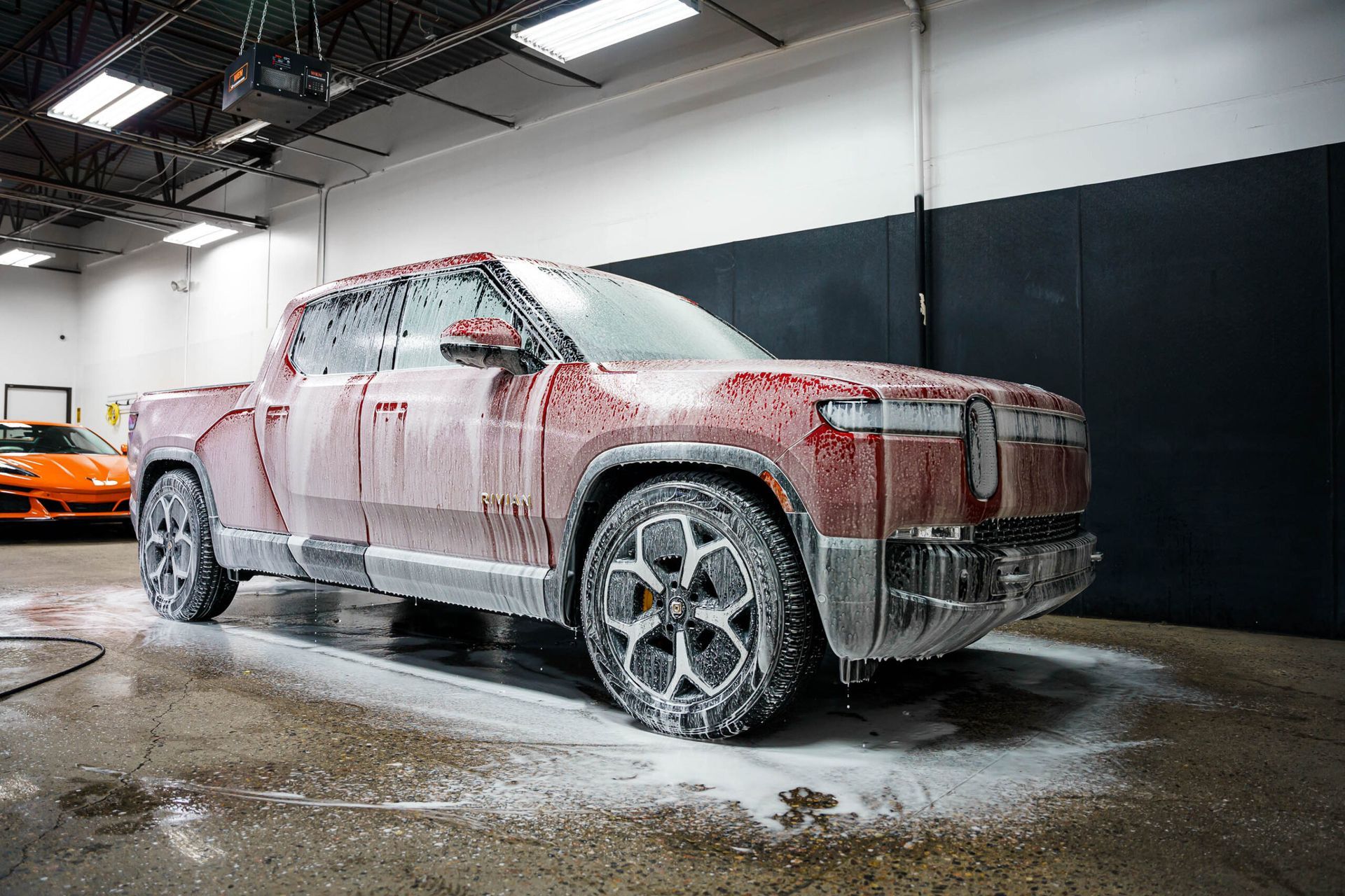 A red truck is covered in foam in a garage.