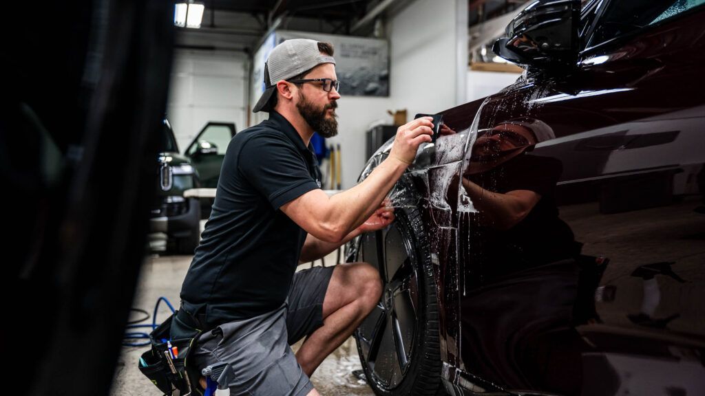 A man is kneeling down to wash a car in a garage.