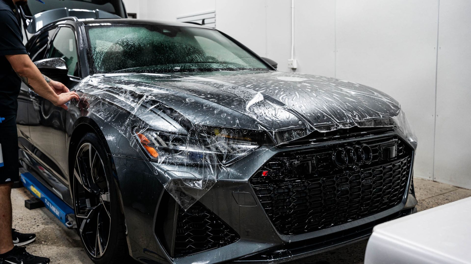 A man is covering a car with plastic wrap in a garage.