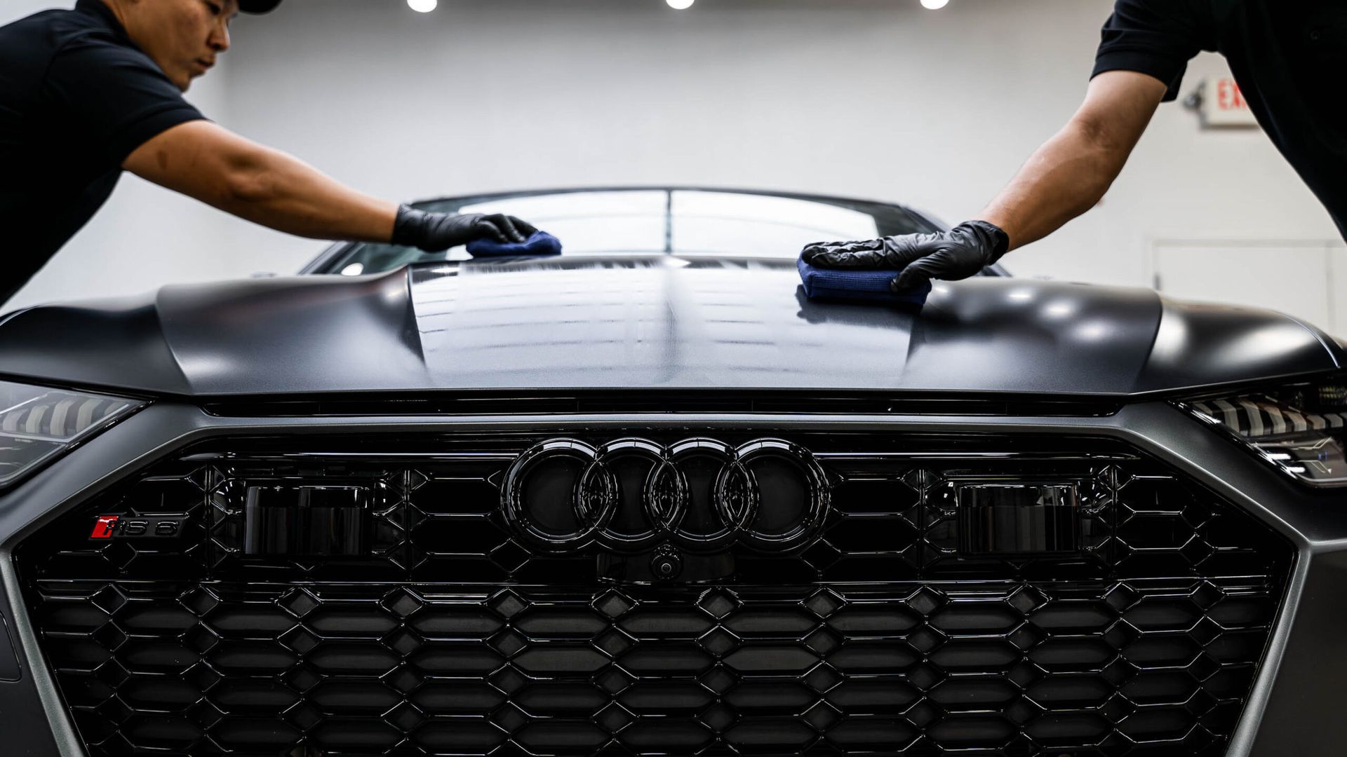 Two men are cleaning the hood of a black car.