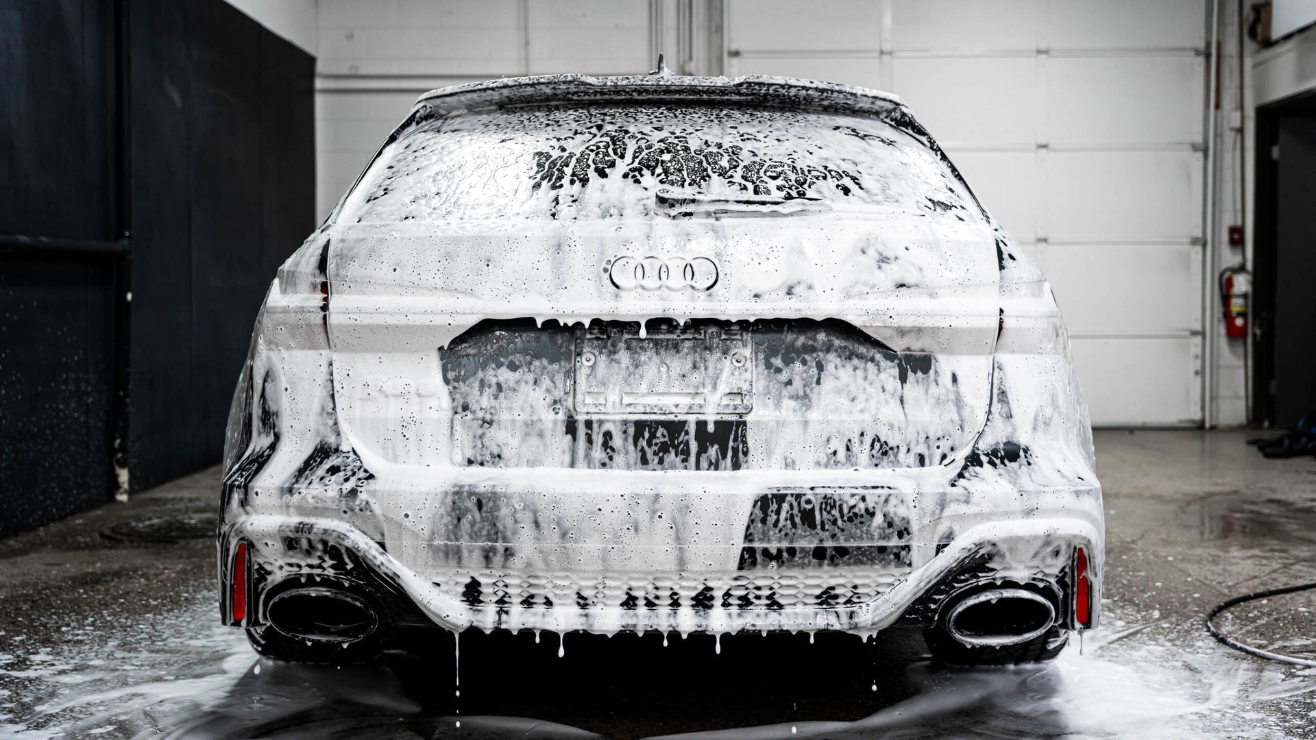 A white car is covered in foam in a garage.