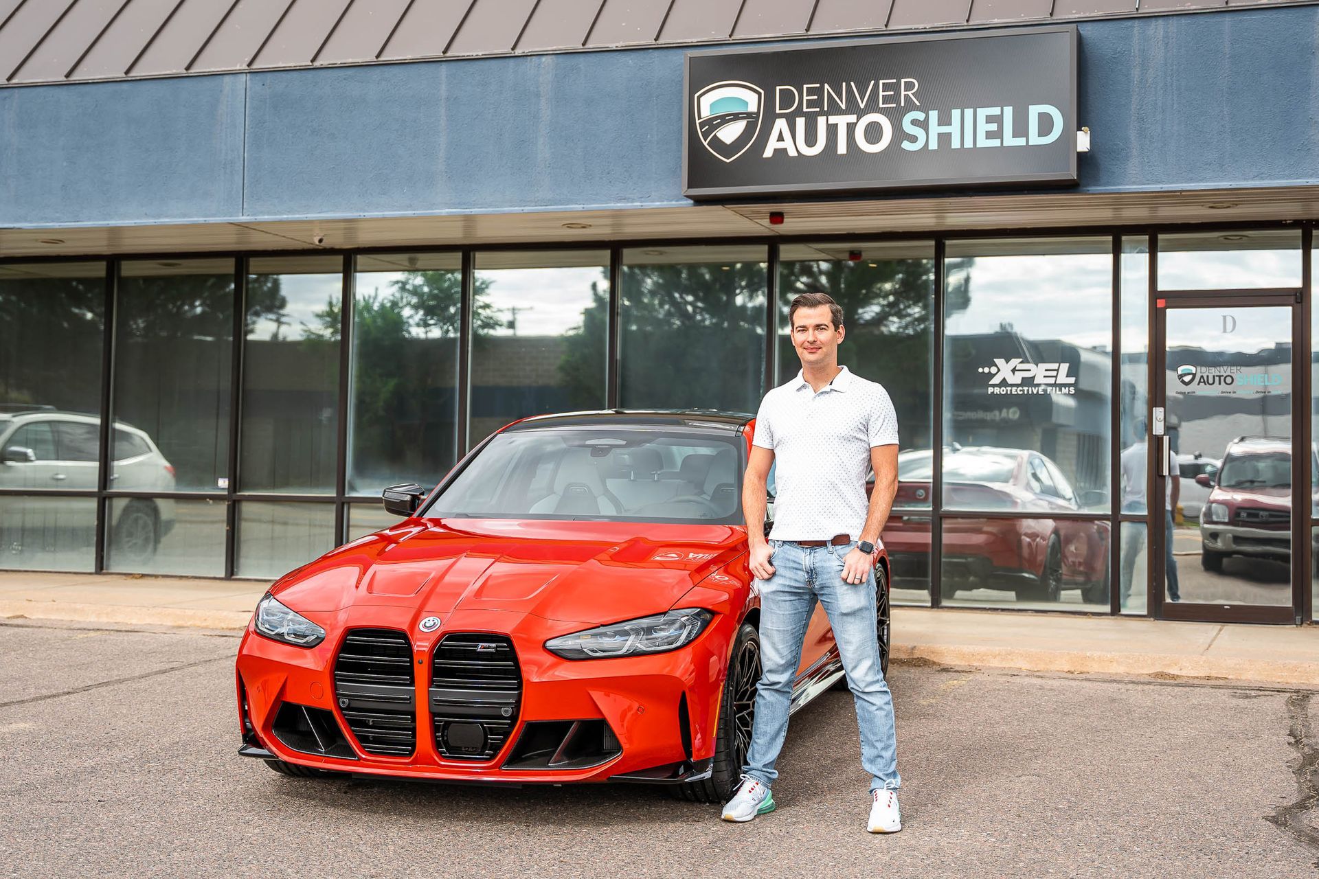 A man is standing in front of a red bmw m4.