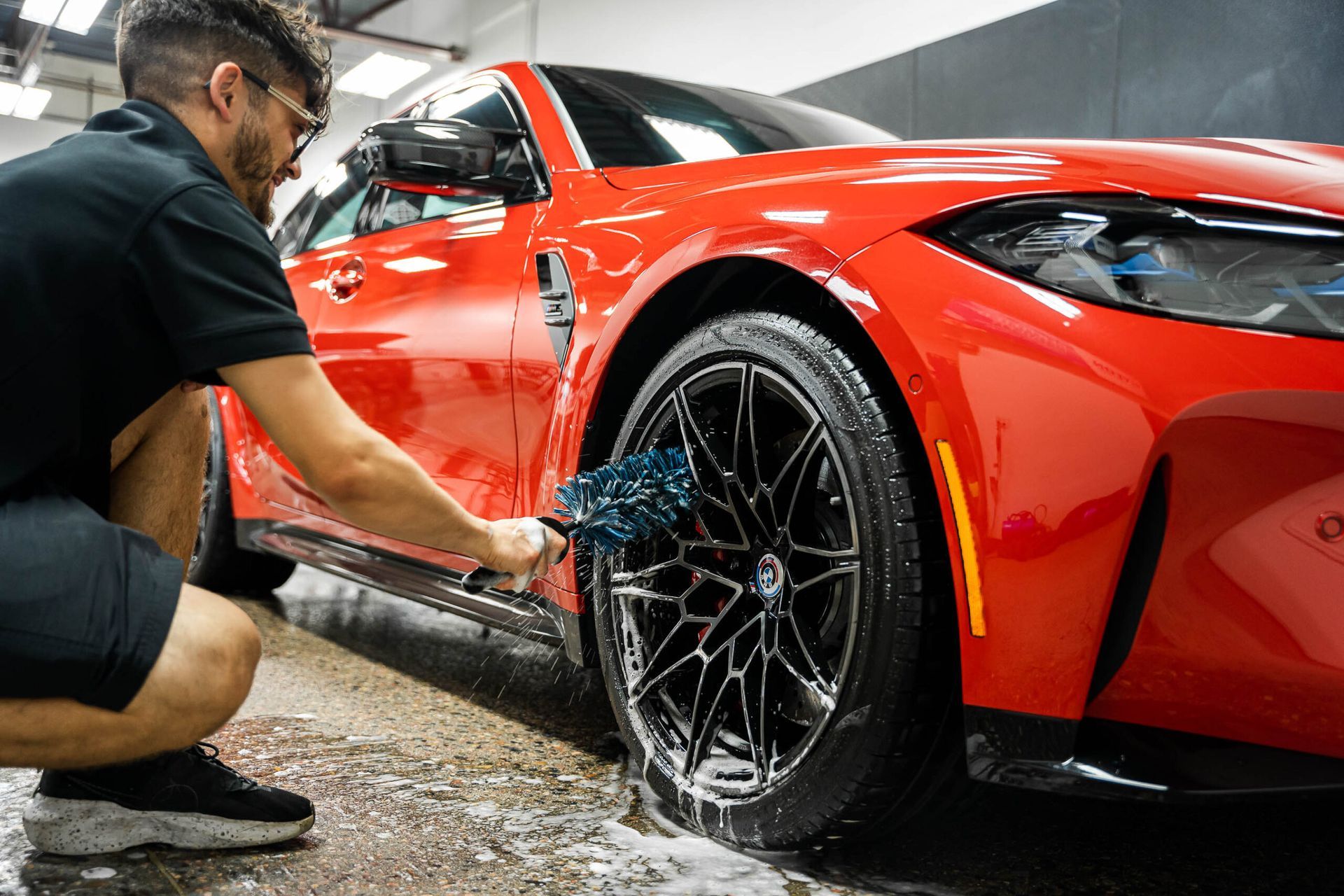 A man is cleaning a red car with a brush.