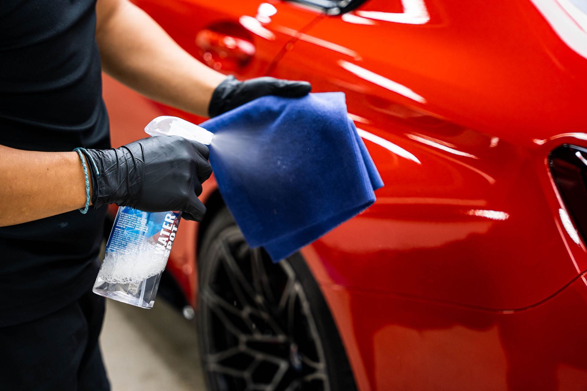 A man is cleaning a red car with a cloth and spray bottle.