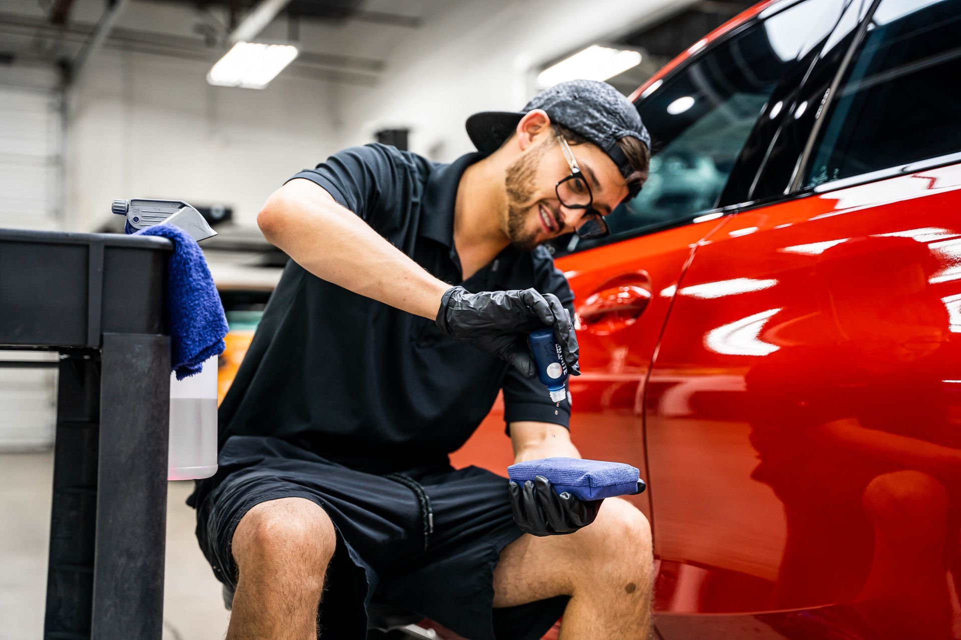 A man is kneeling down in front of a red car.