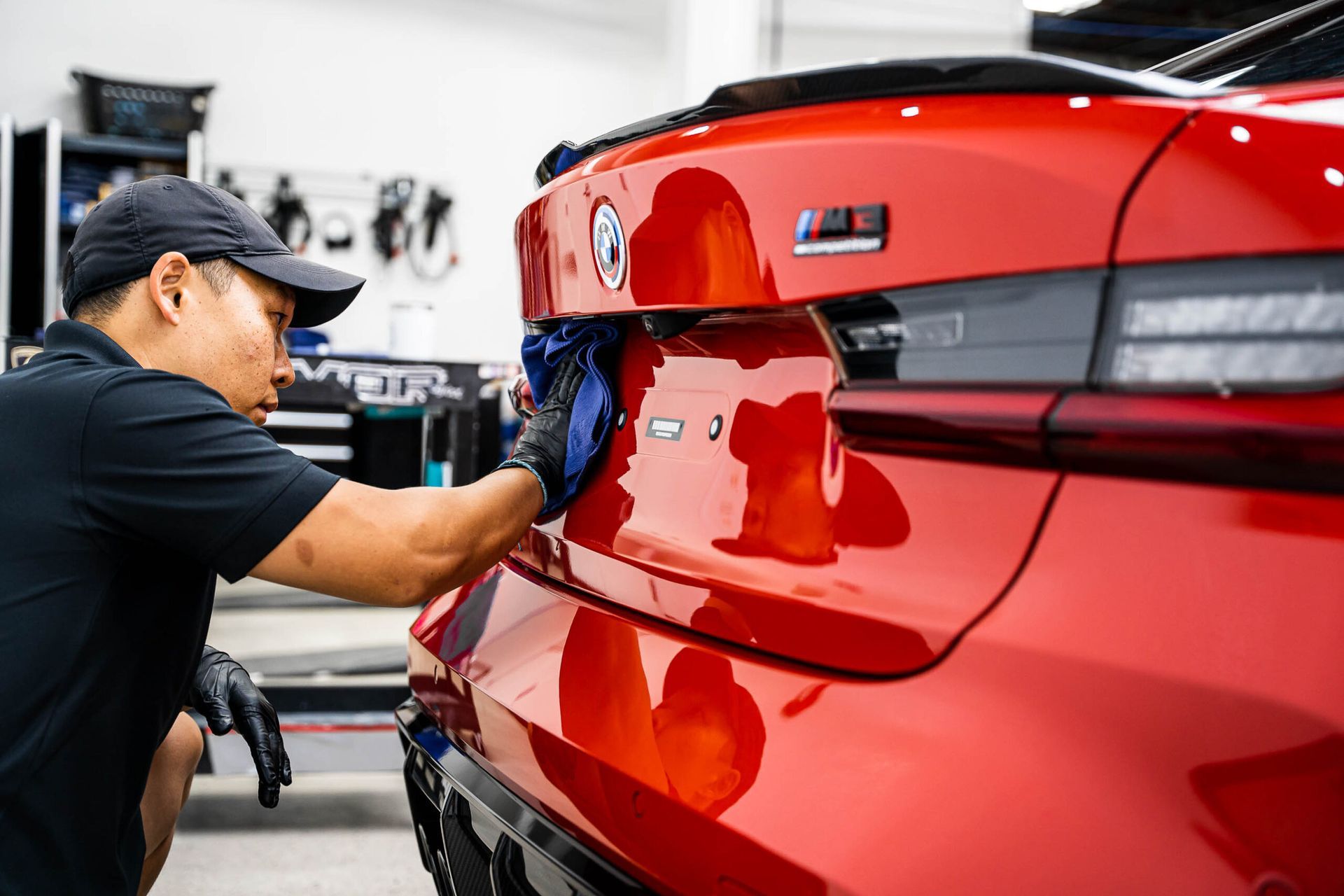 A man is cleaning the back of a red car in a garage.