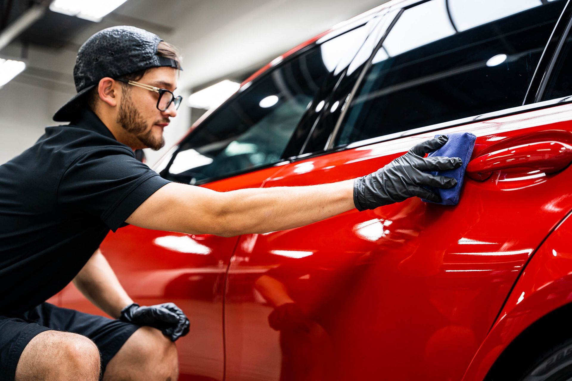 A man is cleaning a red car with a cloth.