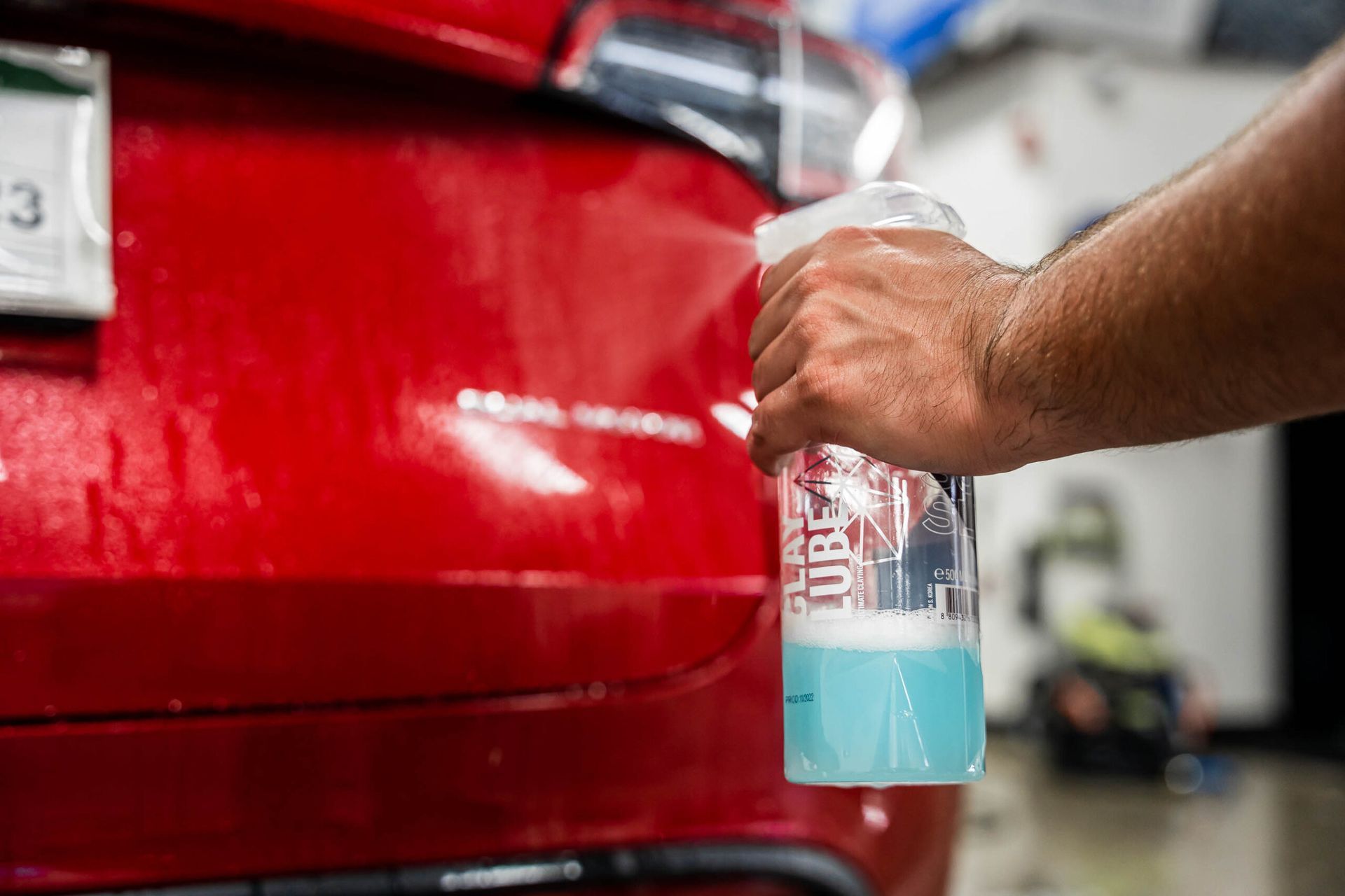 A person is holding a spray bottle in front of a red car.