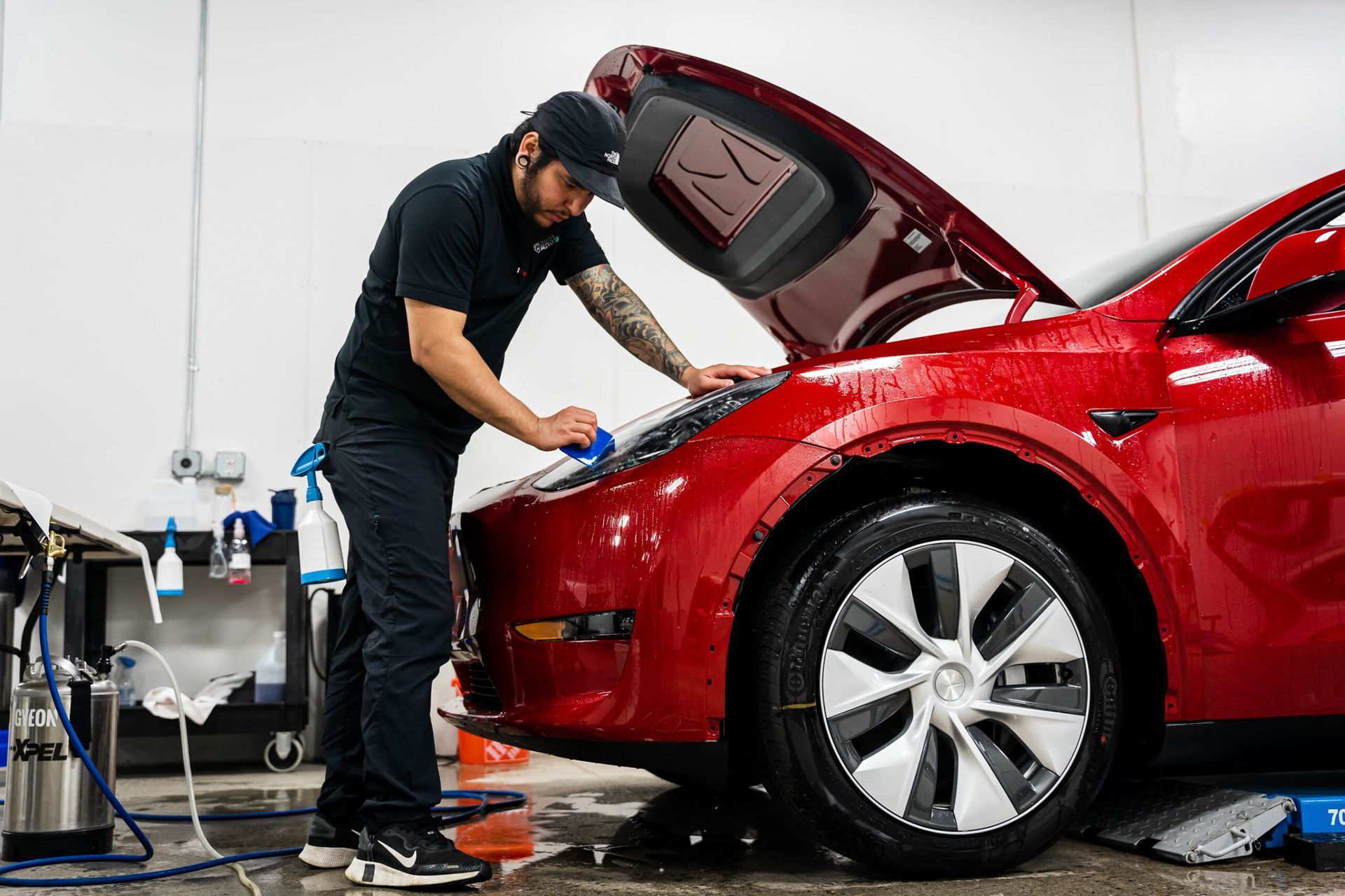 A man is working on a red tesla model y in a garage.