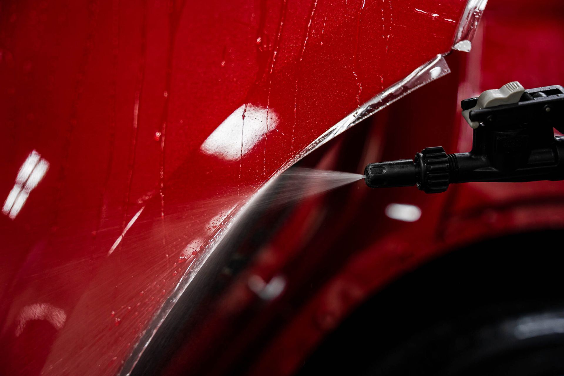 A person is spraying water on a red car fender.