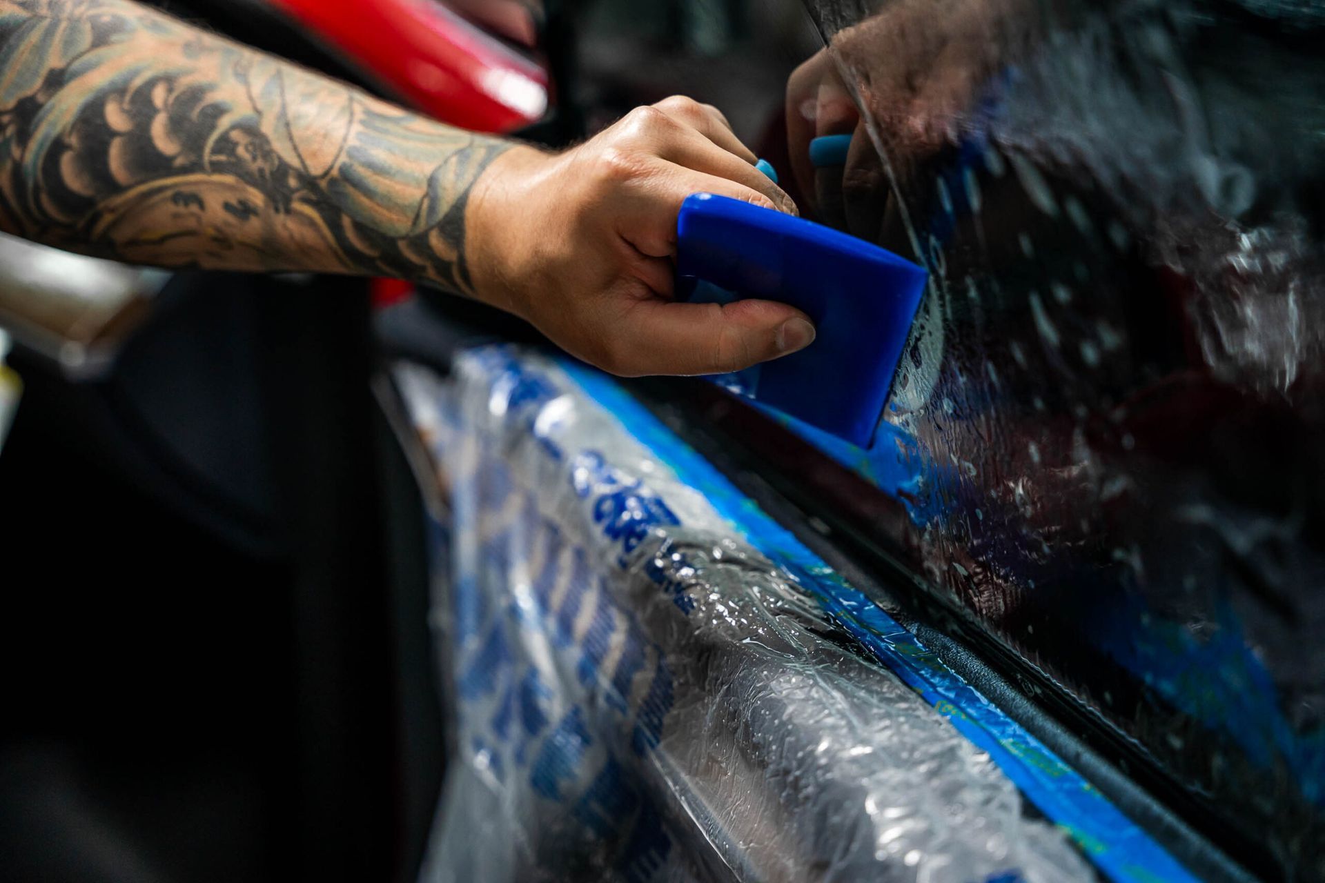 A man is wrapping a car with a blue squeegee.