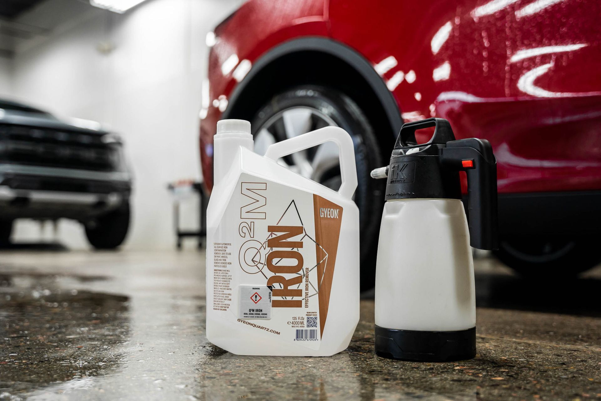 A bottle of iron is sitting next to a spray bottle in front of a red car.