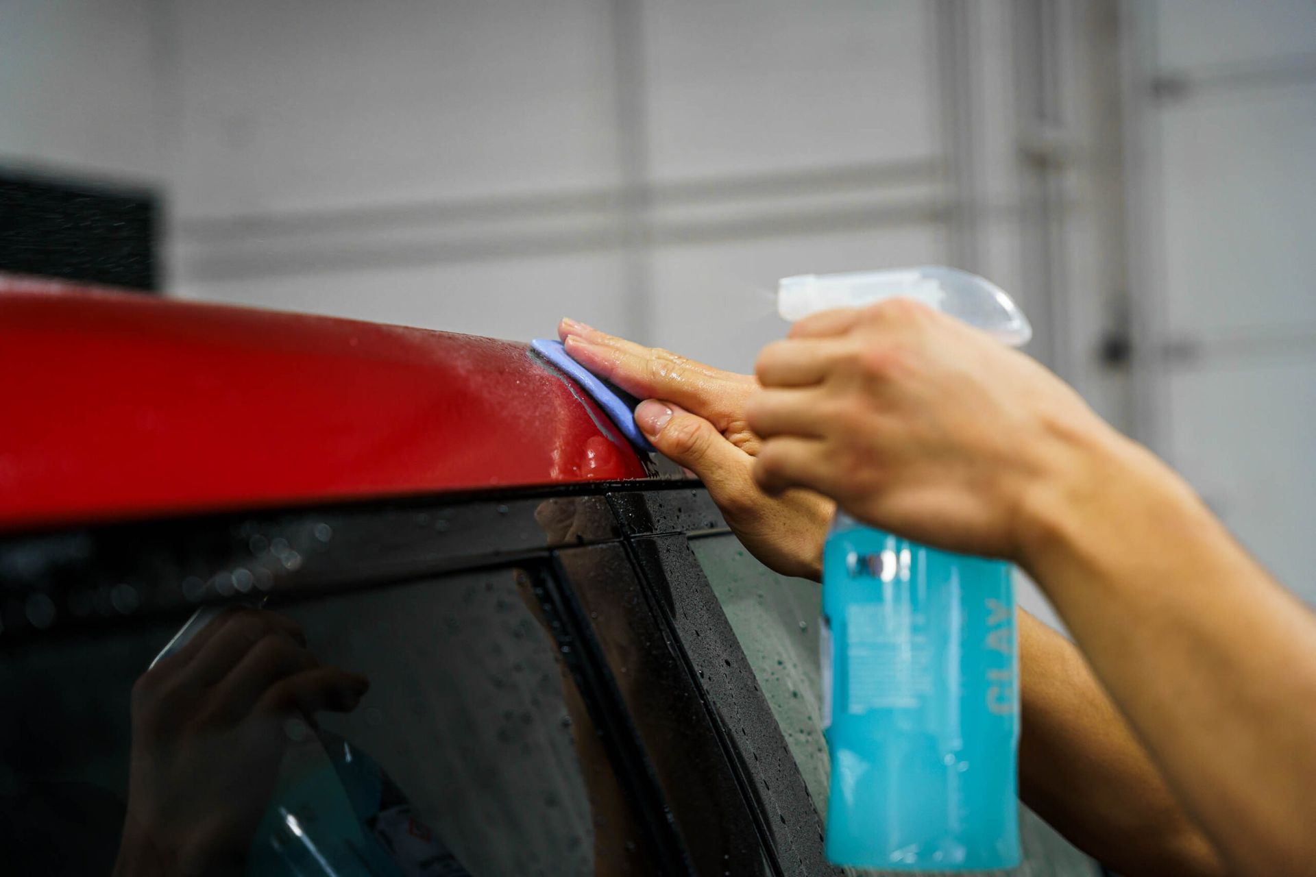 A person is cleaning a red car with a sponge and a spray bottle.