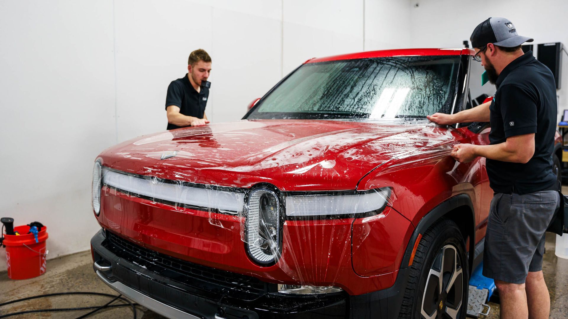 Two men are washing a red car in a garage.