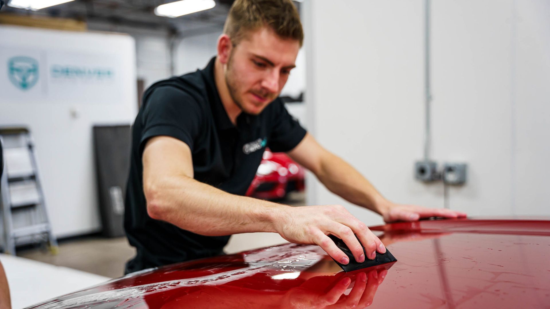 A man is polishing the hood of a red car in a garage.