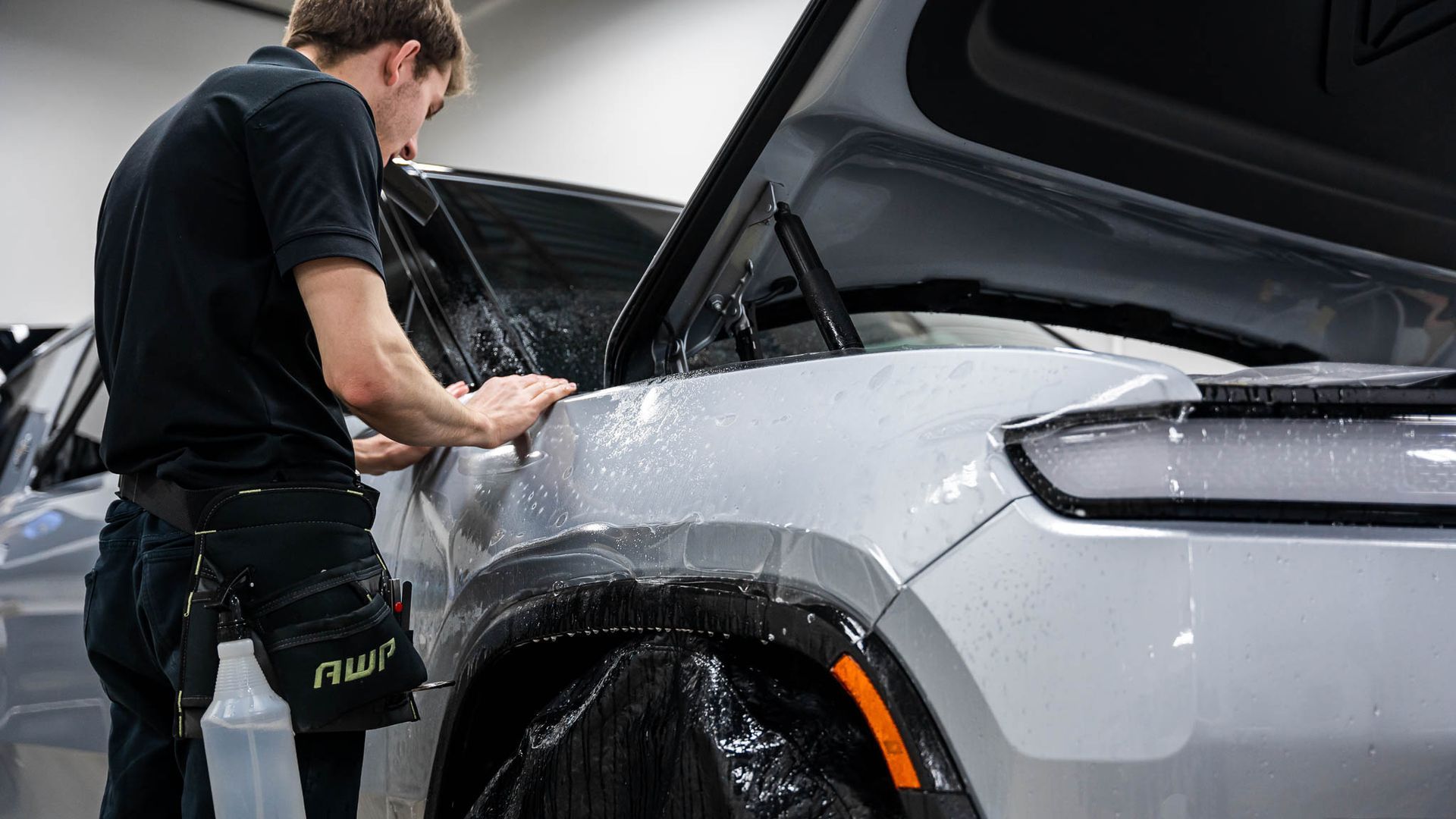 A man is applying a protective film to the fender of a car.