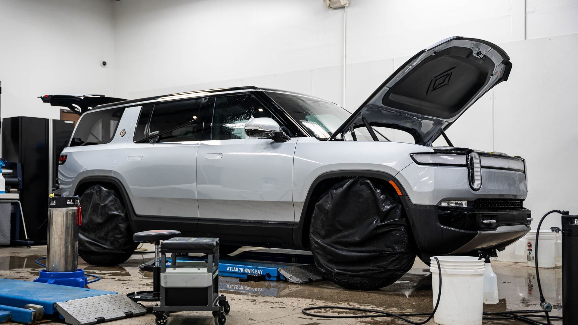 A silver suv is parked in a garage with its hood open.