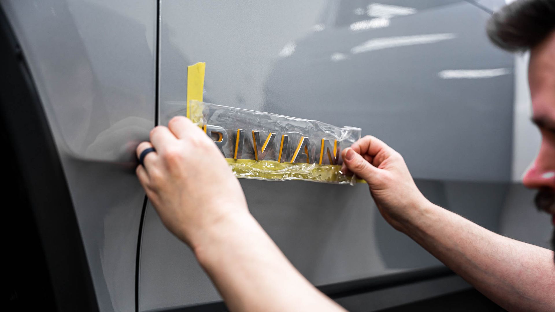 A man is putting a sticker on the side of a car.