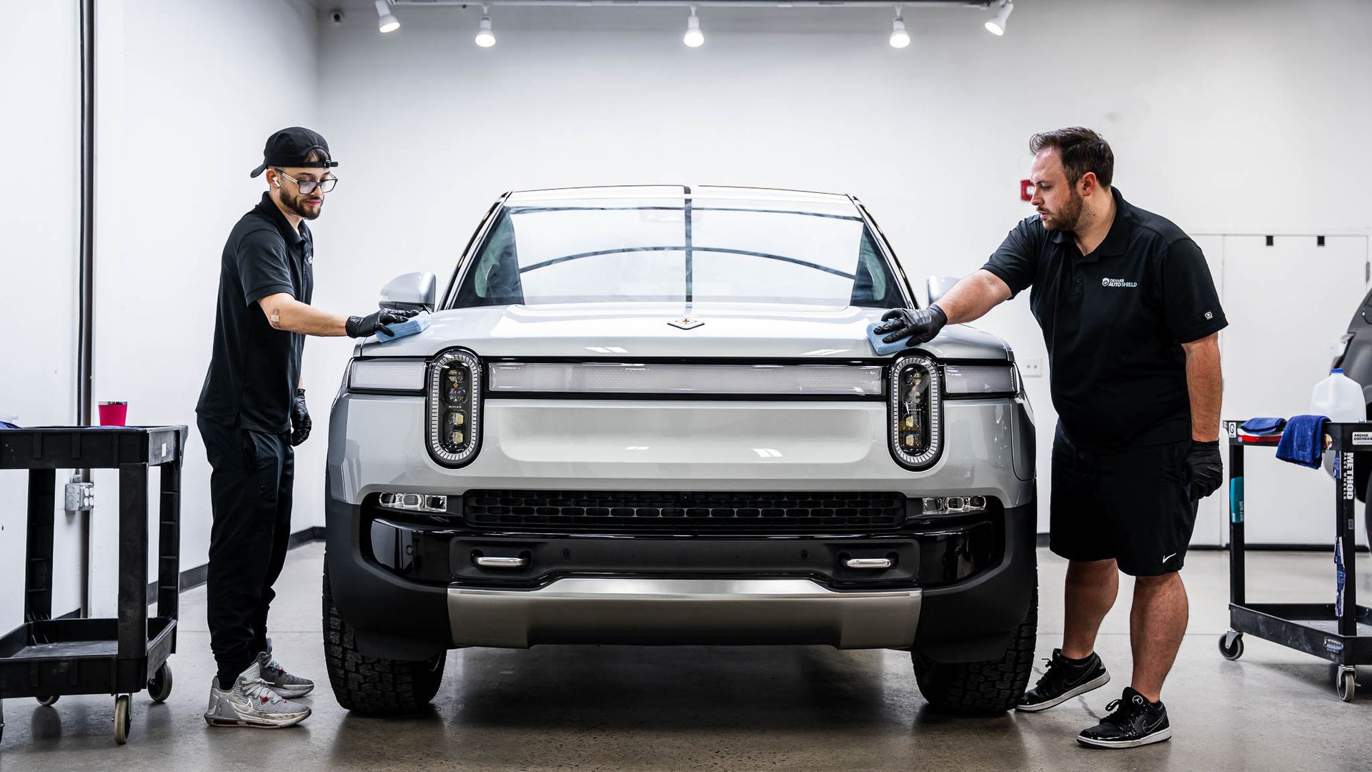 Two men are working on a silver truck in a garage.