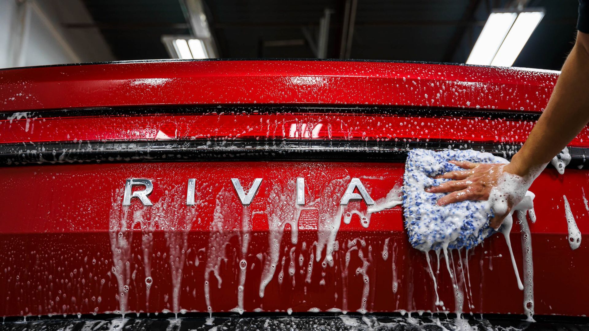 A person is washing a red car with a sponge.